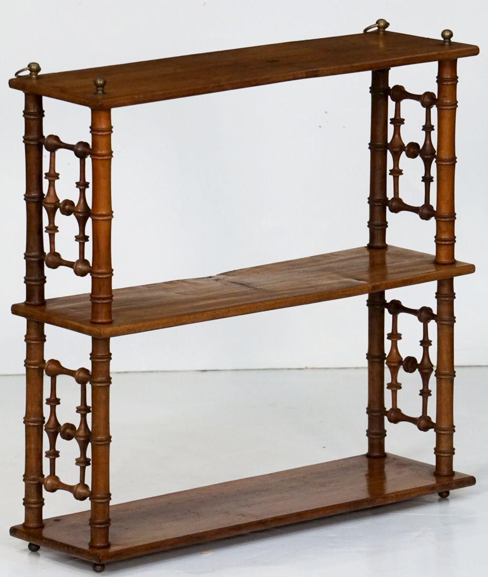 A fine French hanging curio shelf of walnut, from the Aesthetic Movement period, c.1880, featuring three shelves adjoined by turned wood faux bamboo supports, with brass accents above the top shelf.