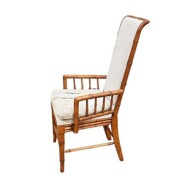 A Hollywood Regency style or chinoiserie faux bamboo upholstered armchair by American of Martinsville. The frame of this chair is created from light brown faux bamboo. The top of the back curls softly back and is framed with faux bamboo. The chair