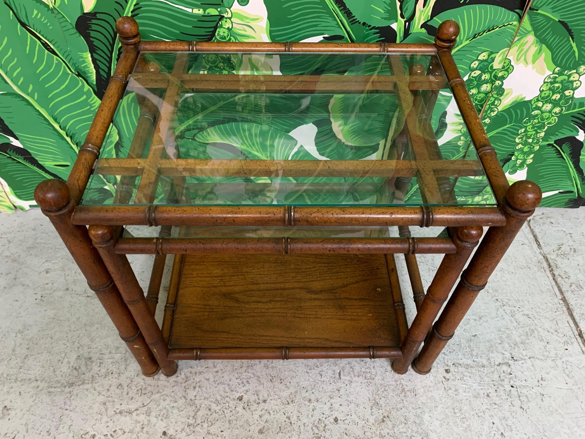 Pair of wood faux bamboo nesting tables feature fretwork detailing and glass tops. Very good condition with minor imperfections consistent with age.