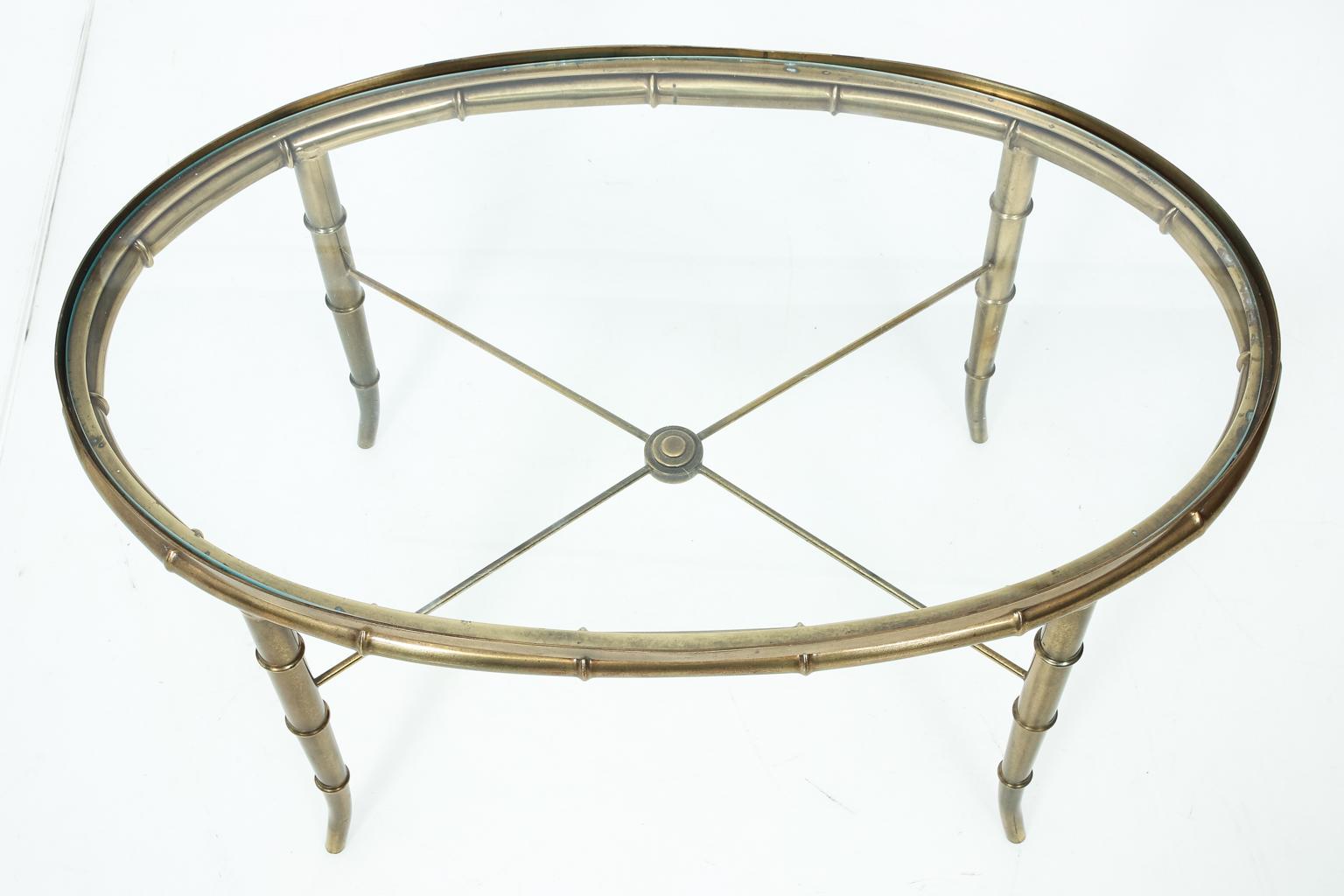 Oval brass table with glass top and bottom X-shaped cross stretcher, circa mid-20th century. Please note of wear consistent with age due to daily use seen on the legs.