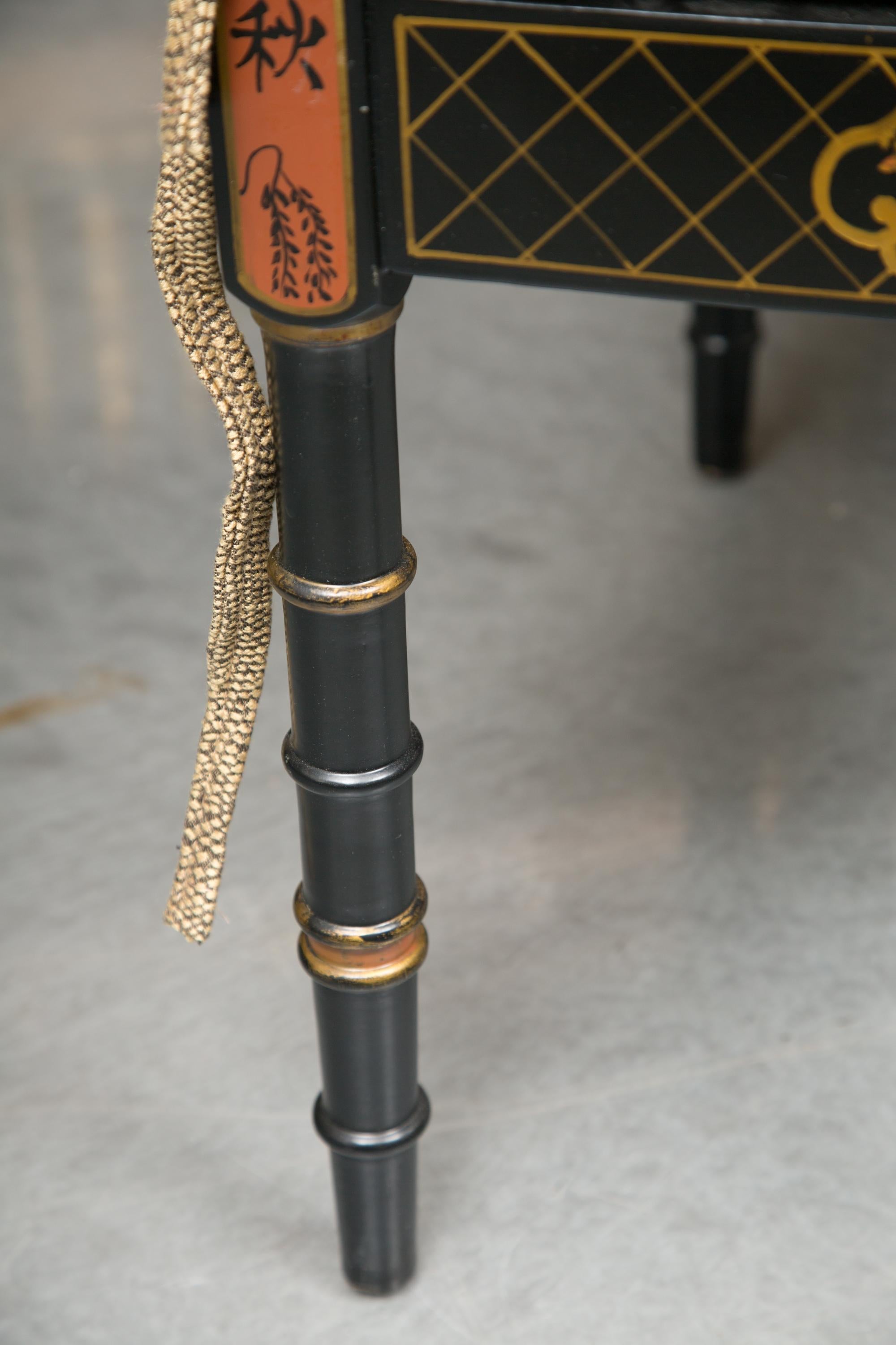 This is a delicate ebonized faux bamboo bench painted overall with chinoiseries. The cane seat is covered by a loose cushion, 20th century.