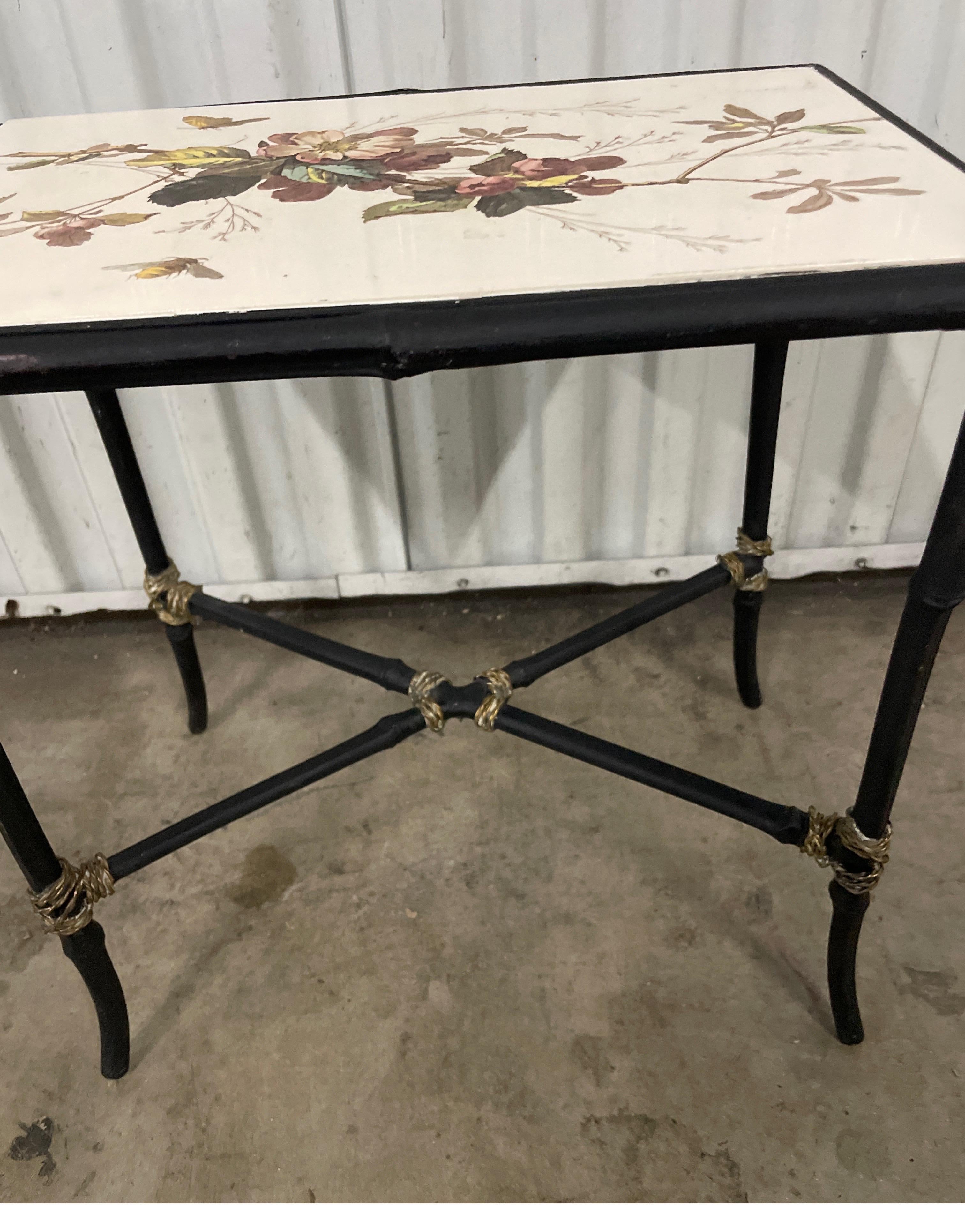 Faux bamboo wrought iron side table with brass tie accents. Top is a painted porcelain tile with flowers and butterflies. A sweet little drinks table.