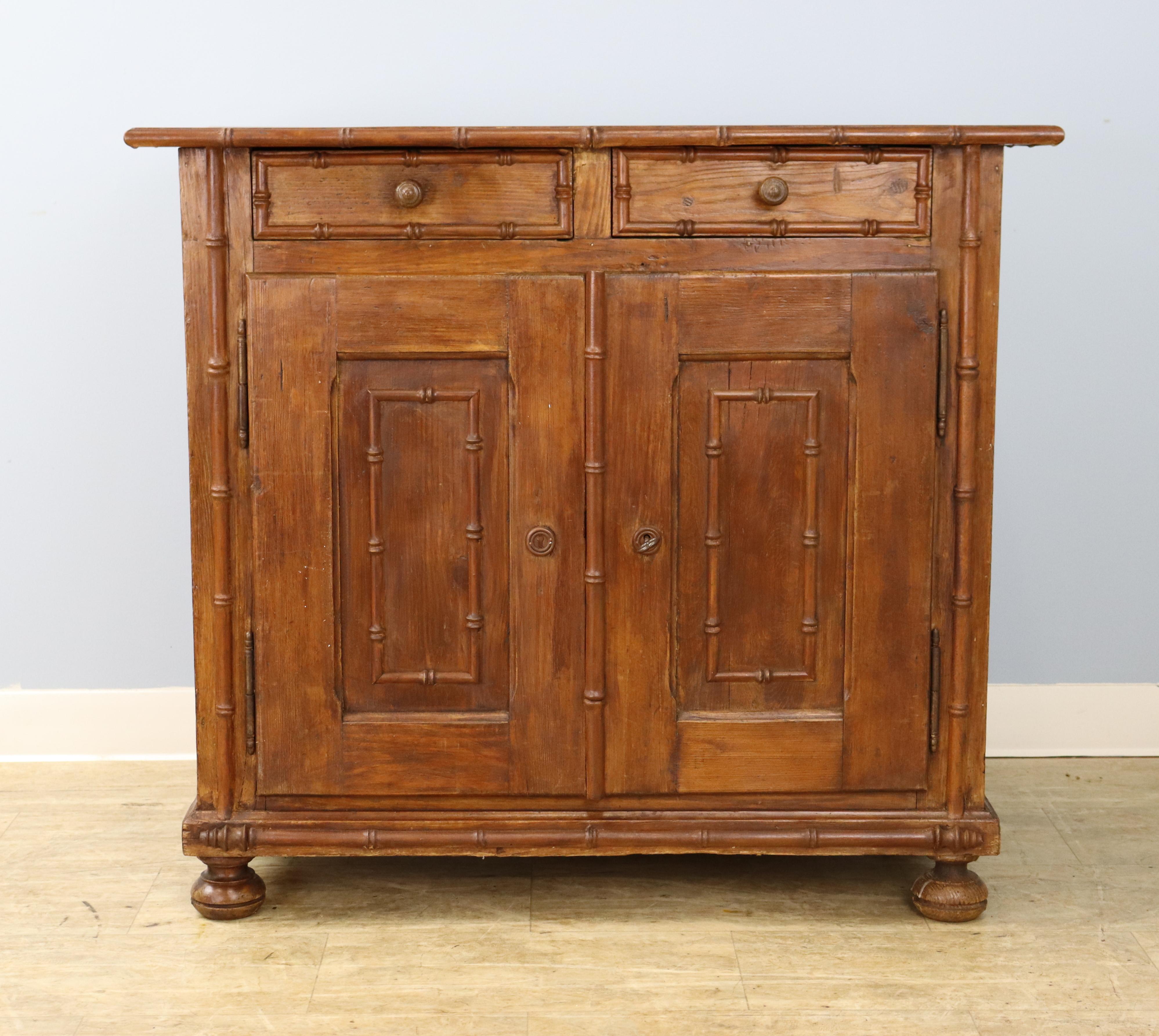 A charming country cupboard in honey colored pine with good faux bamboo details. Two roomy drawers at the top, with a single non adjustable shelf in the cupboard. Note: This piece appears to have been previously used for electronics and has two