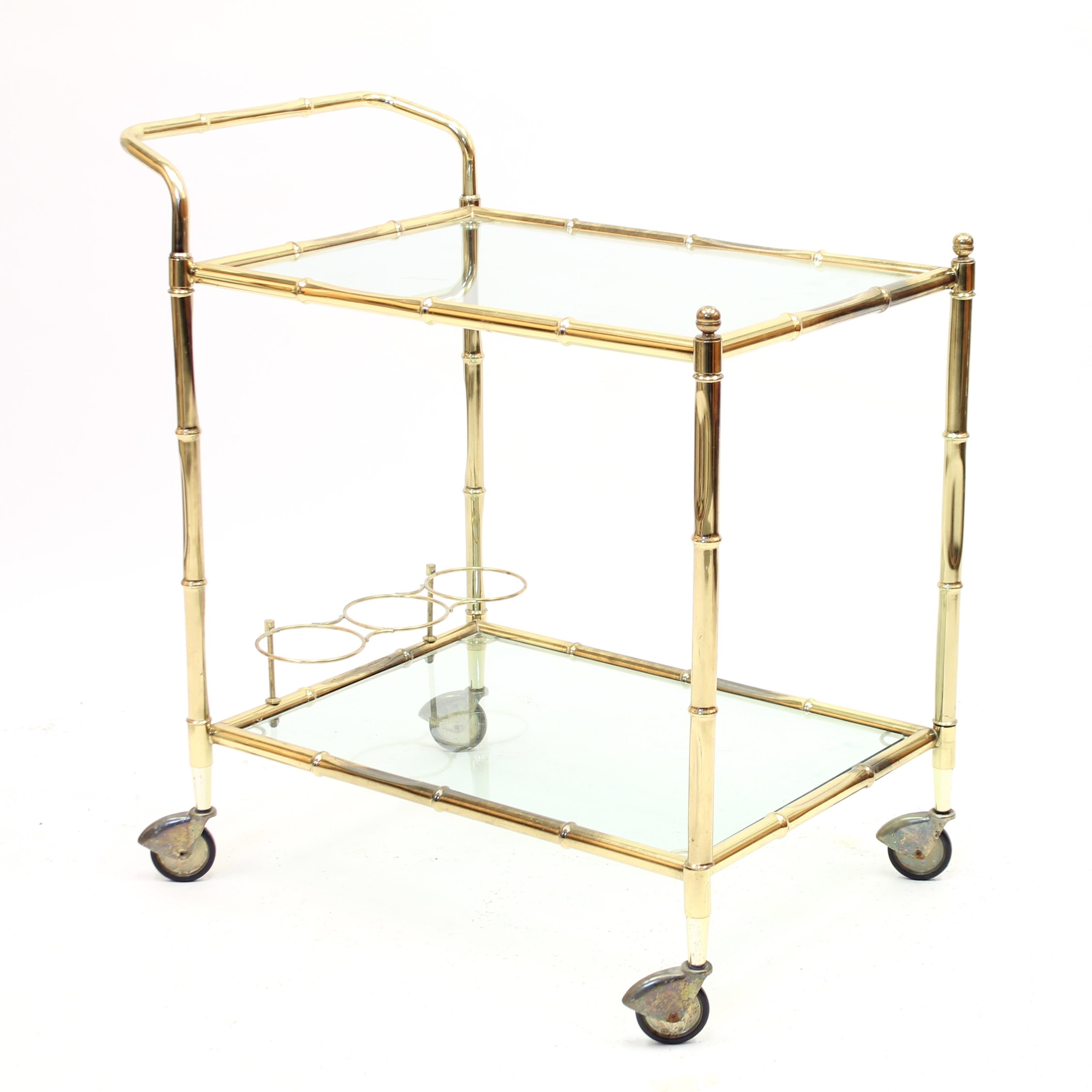 Brass bar cart / trolley with bambu shaped tubular brass rods that makes up the frame. Two levels with glass shelving and lower level with holder for three bottles. Good vintage condition with light ware and patina consistent with age and use.