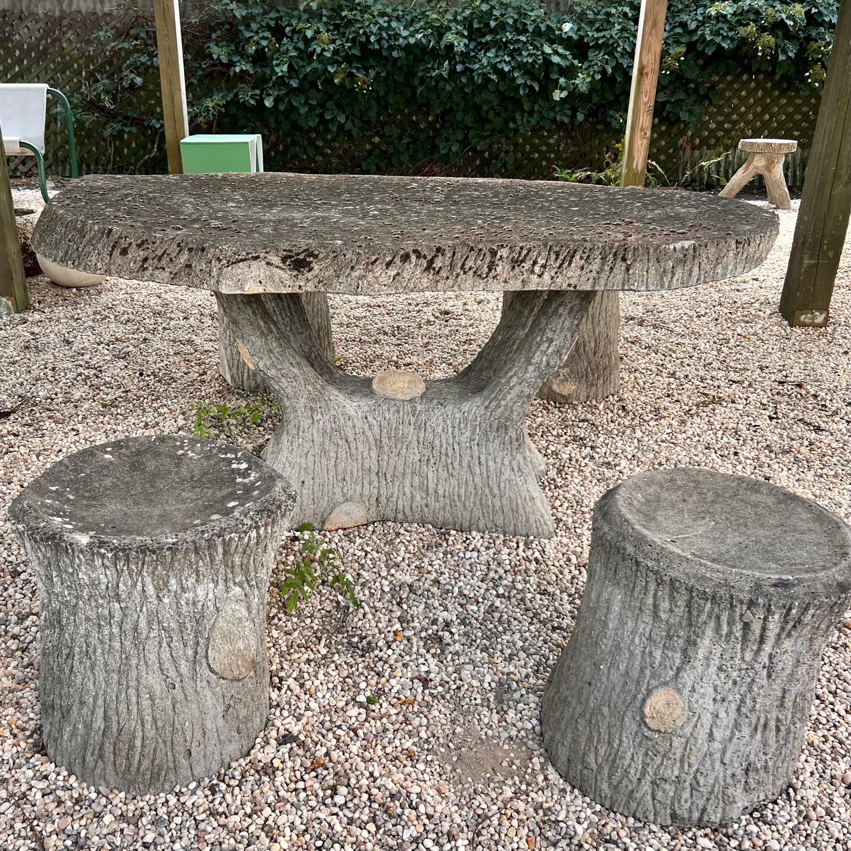 Substantial faux-bois concrete table and stools from France, made in the 1960s. 4 stools and one table included in this set. Legs and table base resemble tree trunks and branches. Oversized tabletop covered in lichen, moss and patina sits atop the