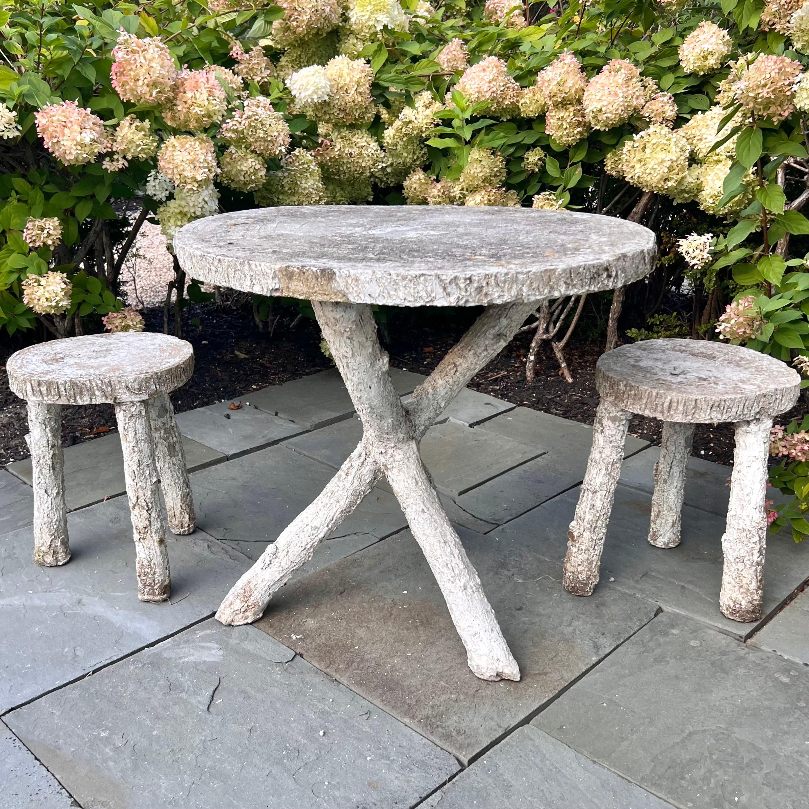 Stunning faux bois concrete table and matching stools from France, made in the 1960s. 2 tripod stools and one tripod table included in this set. The table features long crossed legs at the base with a brutalist design. 2 tripod stools easily stow