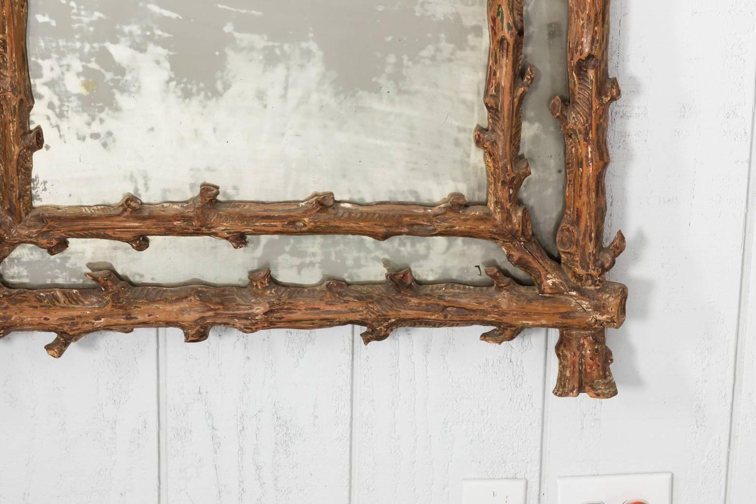 Carved faux bois mirror with smokey glass and is capped with a faux boix pediment design, circa 20th century.