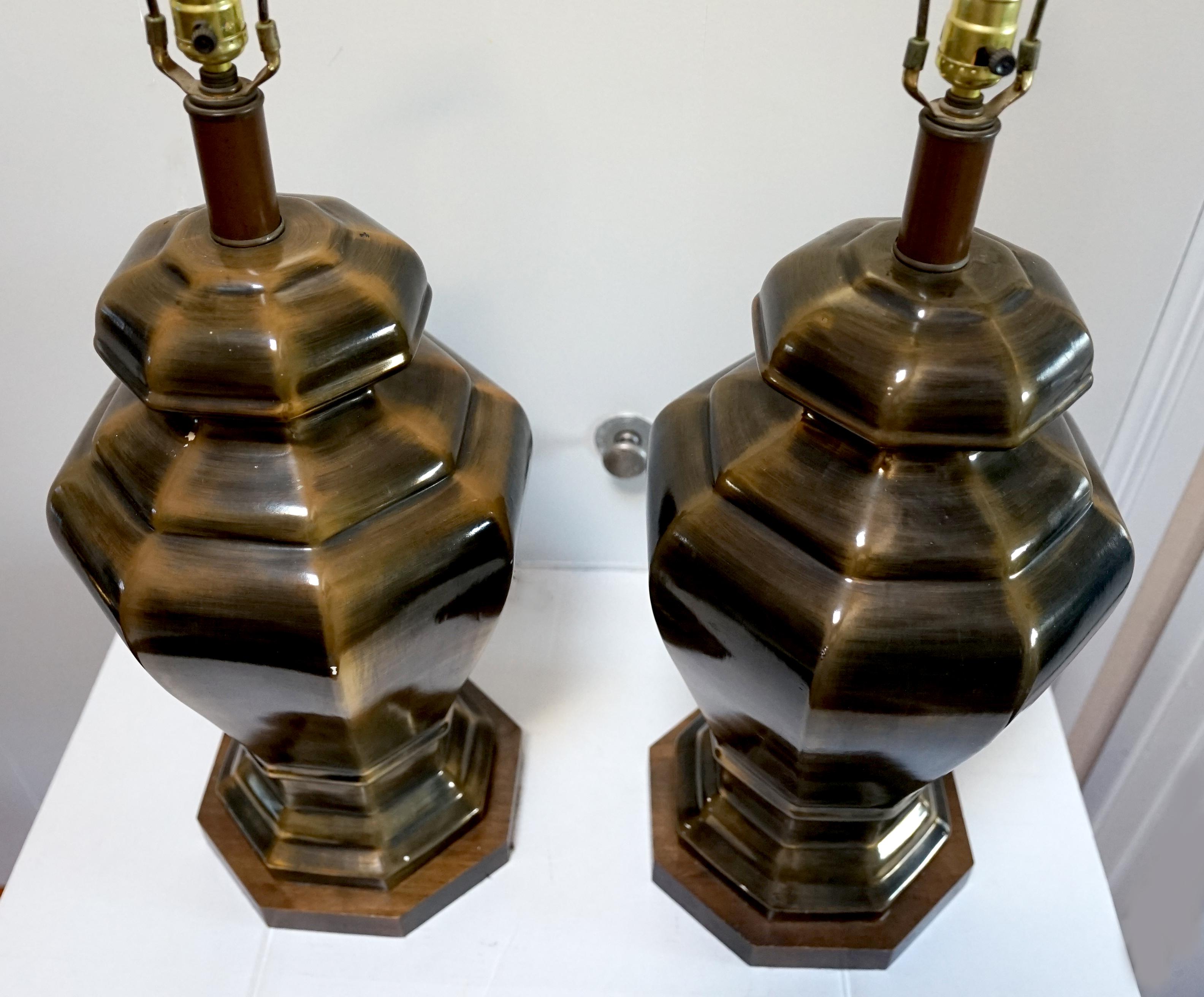 The appearance of brass in this pair of oversized lamps makes them difficult to resist. The lamps are faux brass, although they are ceramic with a wood base. This pair of vintage hexagonal lamps are mid-century pieces and quite rare.  
Each has a