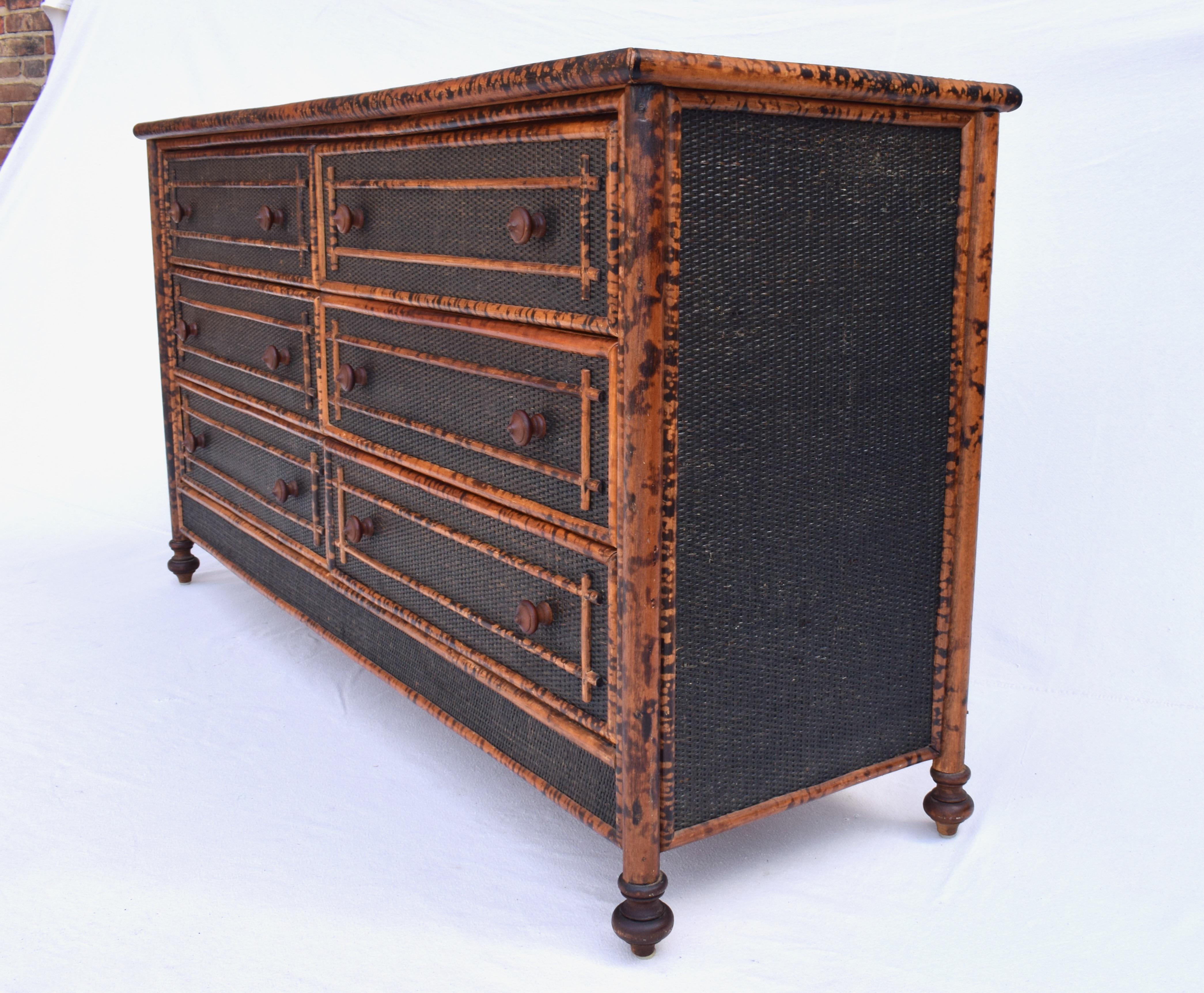 British Colonial style midcentury chest of six drawers covered in black grass cloth with striking burnt tortoise bamboo frame. An especially handsome piece featuring turned wood pulls and feet as seen in period British Colonial furniture. Ready for