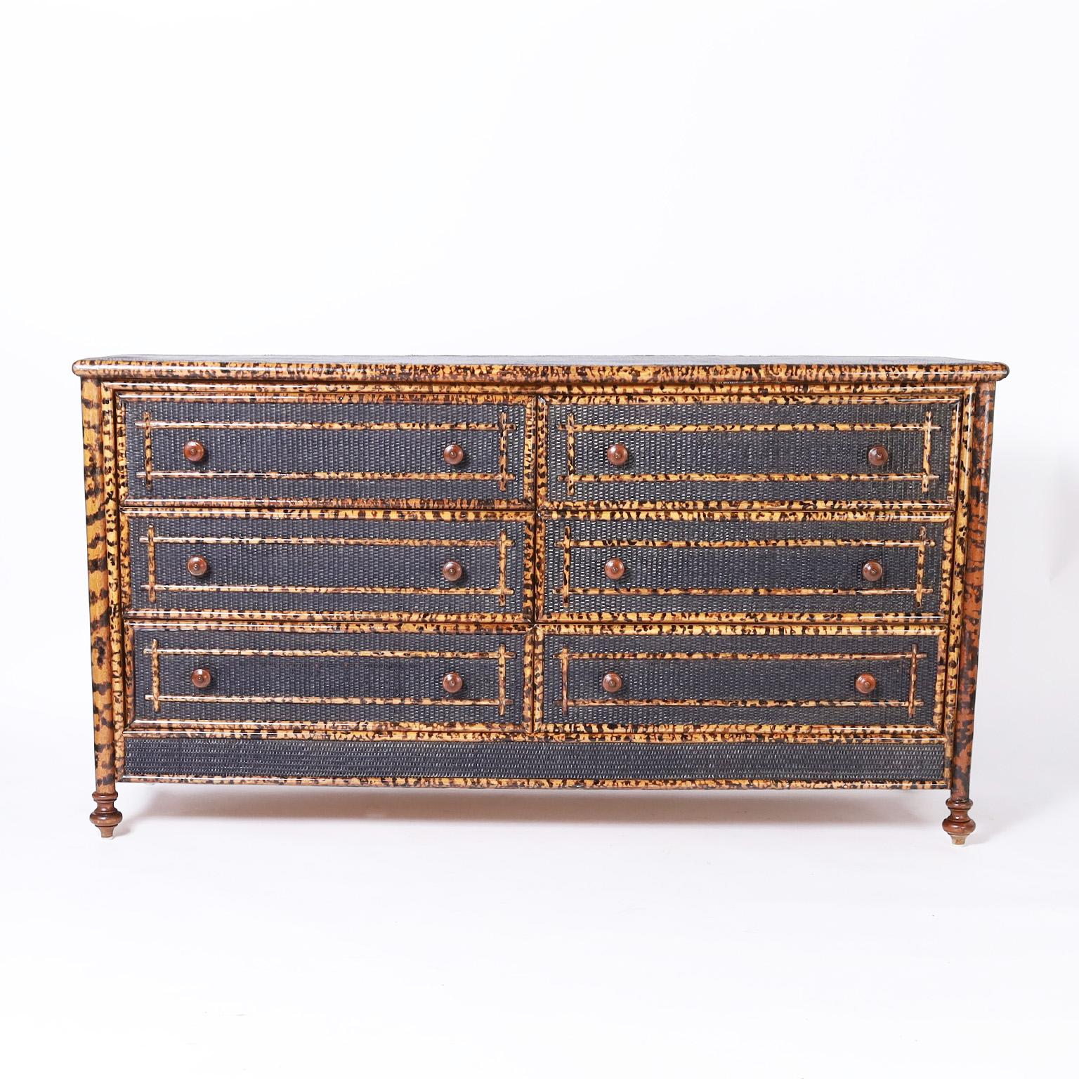 British Colonial style mid century chest of six drawers with a faux burnt bamboo frame, black painted grasscloth panels with applied bamboo designs and turned wood pulls and feet.