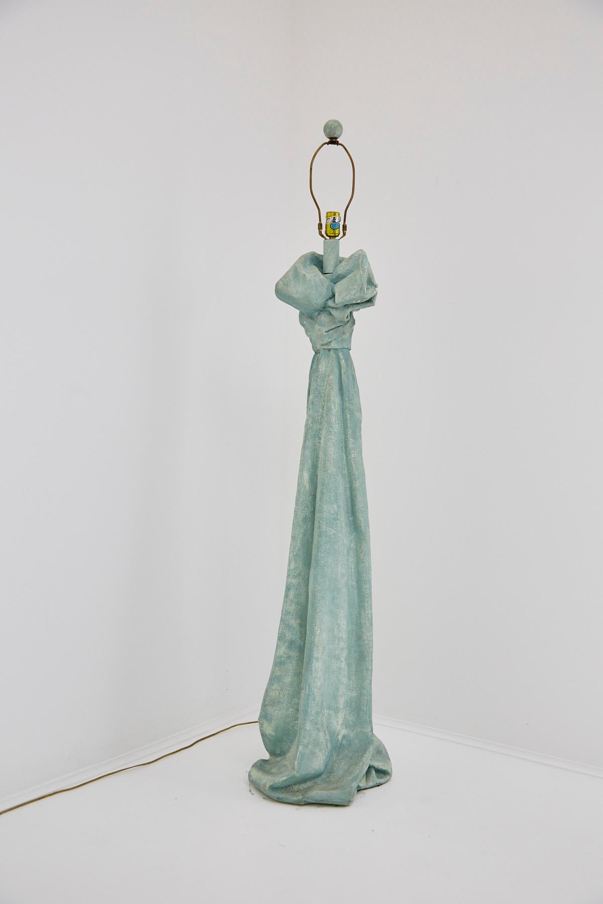 Sculptural floor lamp comprised of composite body in the form of draped and bow-tied fabric in the style of John Dickinson. Wooden neck and original wooden finial. Original light turquoise paint throughout. Very heavy.

Shade not included.