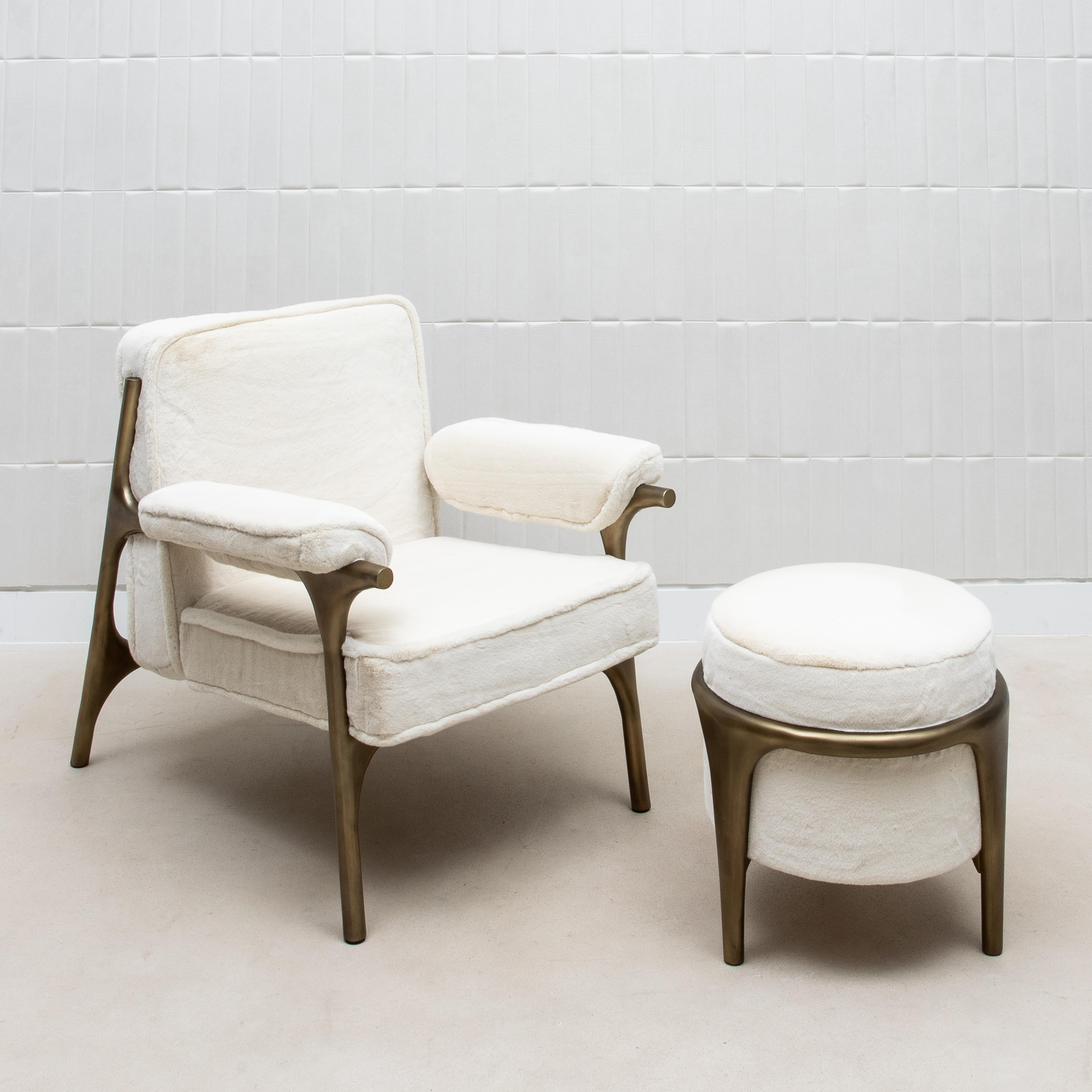The Ramo Chair and Ottoman by R&Y Augousti epitomize the ultimate in luxurious comfort, enveloping you in a cloud of plush, ivory faux fur. The chair’s elegantly contoured frame, crafted from bronze patina brass, adds a touch of timeless