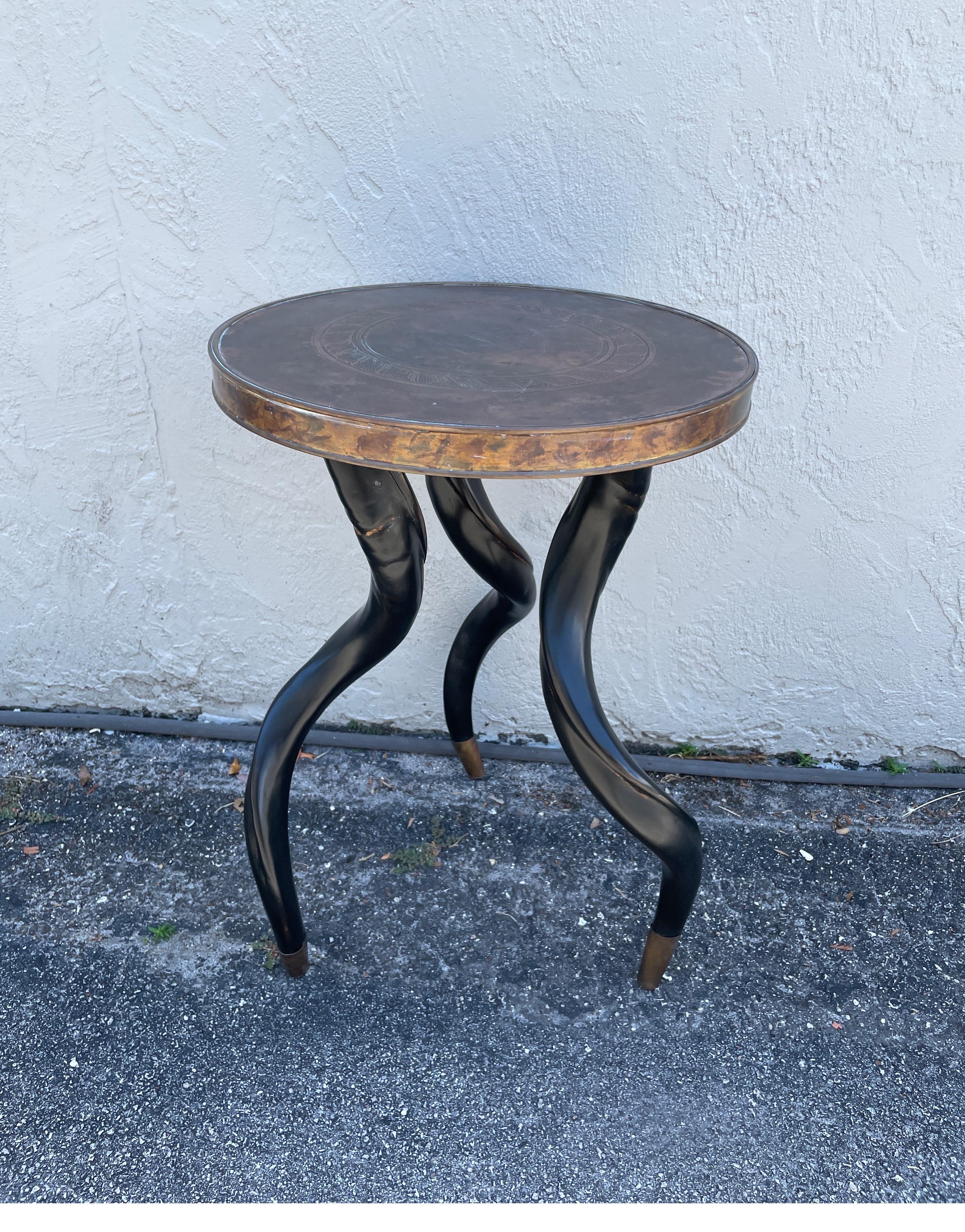 Antiqued brass top table with three ebony faux horn legs with brass tips.