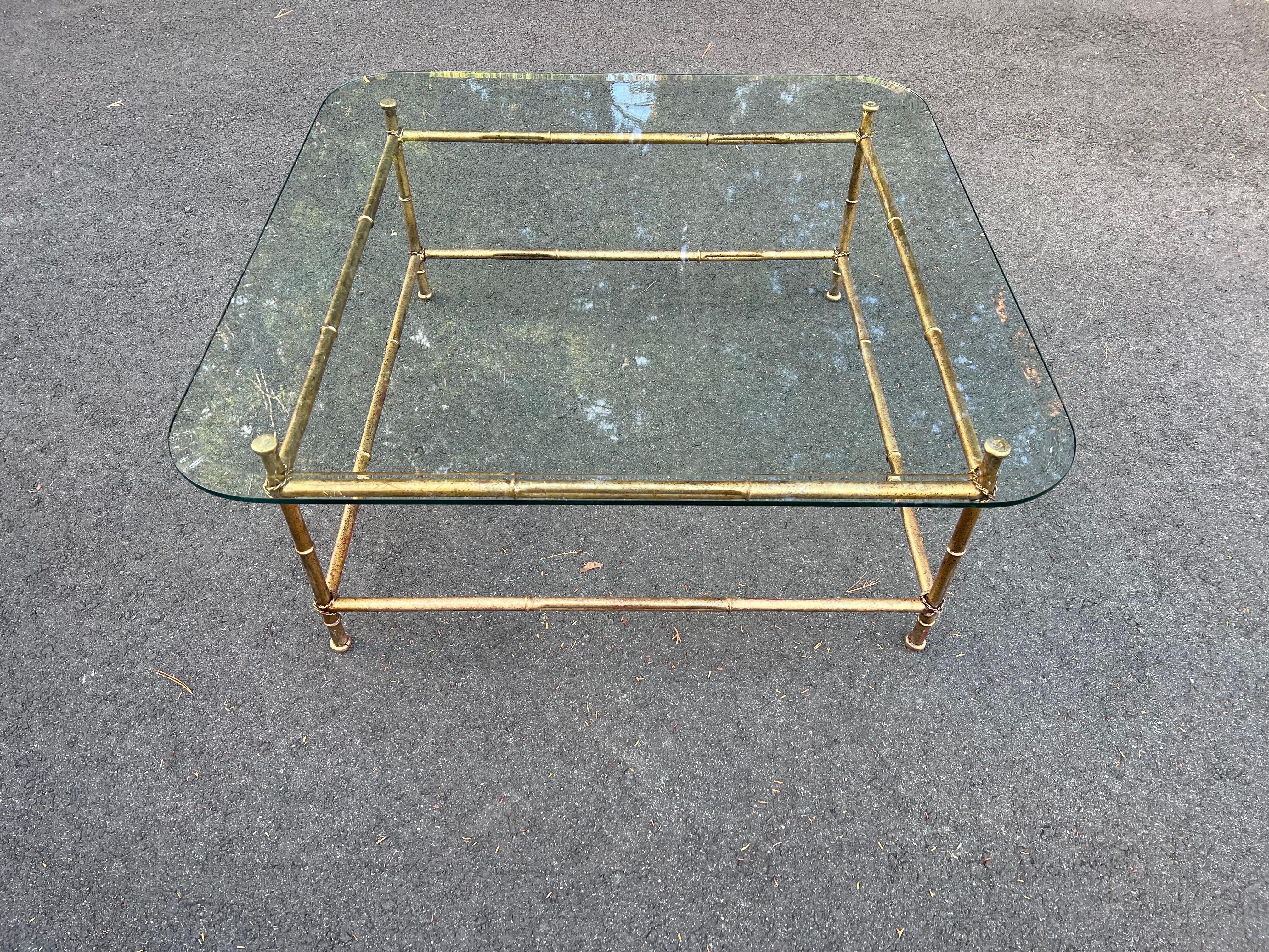 Faux Bamboo Gilt Metal Coffee Table with Glass Top. Nice bevelled glass top with wide rounded square glass design. Rope tassle details around each corner. Classic design and timeless elegance make up this piece.