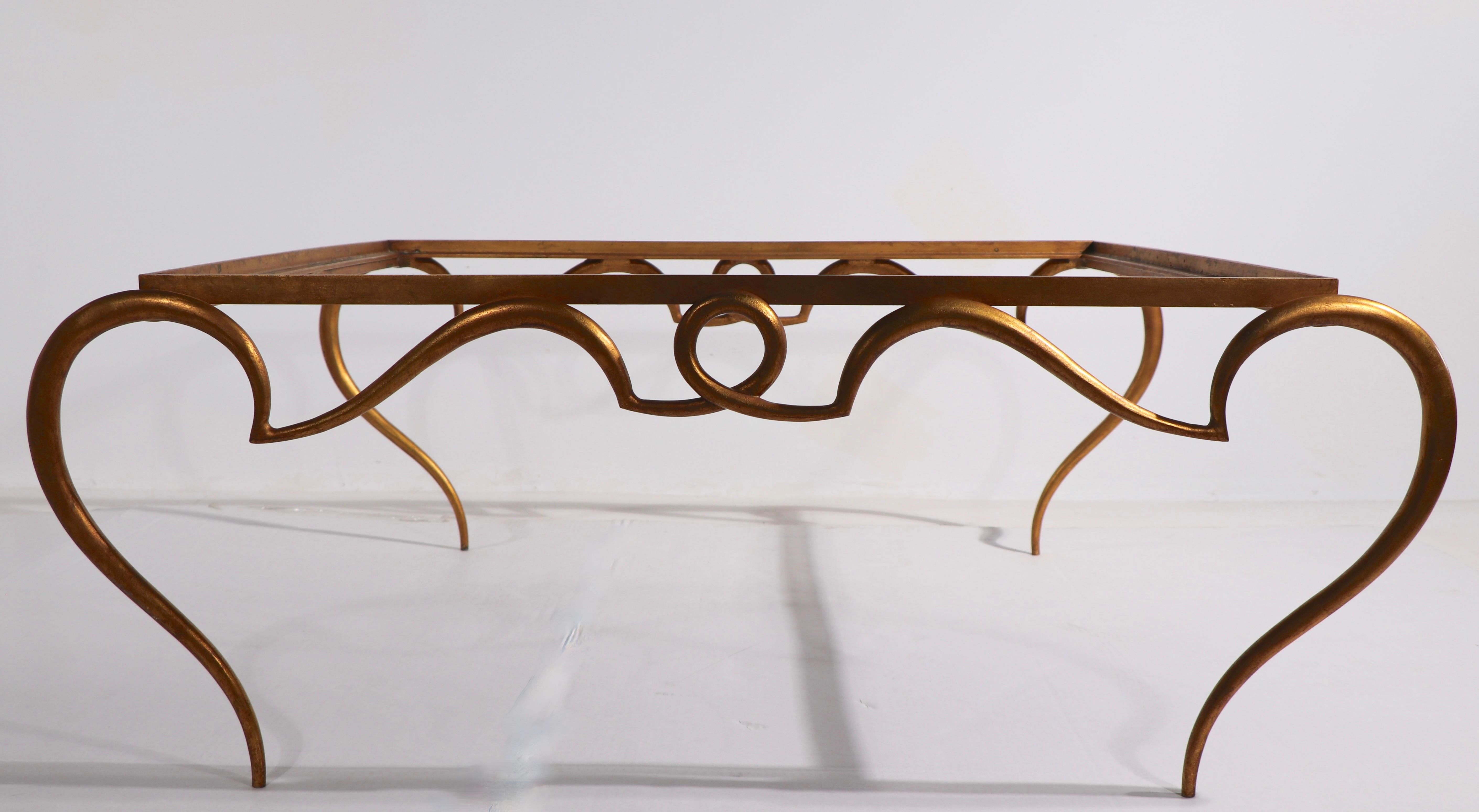Table basse glamour Art Déco, Hollywood Regency en métal et verre. La table est dotée d'une base en métal à volutes et d'un plateau en verre biseauté d'origine. Nous pensons que cet exemple est français, peut-être René Drouet, non signé. Design/One