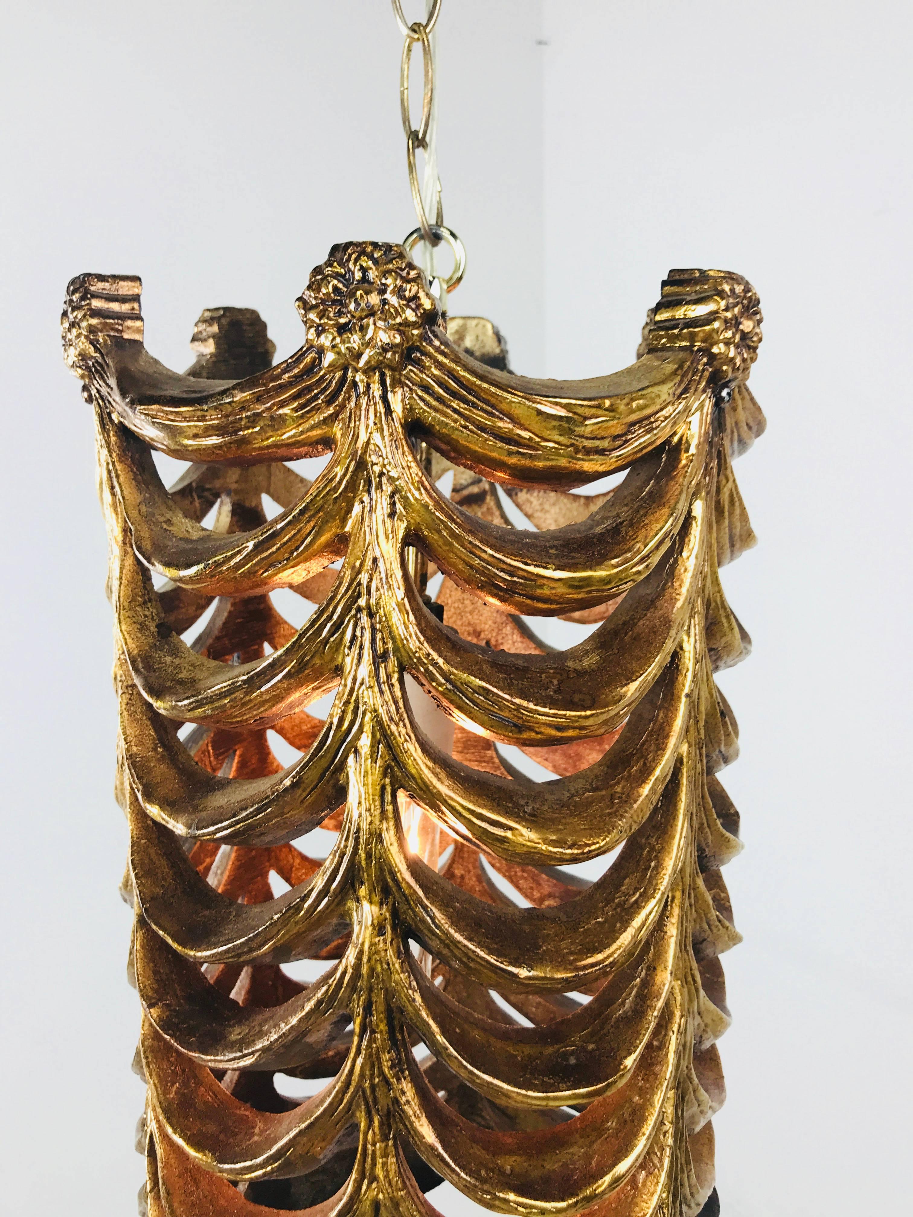 Colgante para cortinas de pan de oro de imitación. Polímero moldeado con guirnaldas de cortinas como cuerpo y rosetas en la parte superior del accesorio. Una sola luz. La luz es un accesorio enchufable y se puede convertir en cableado