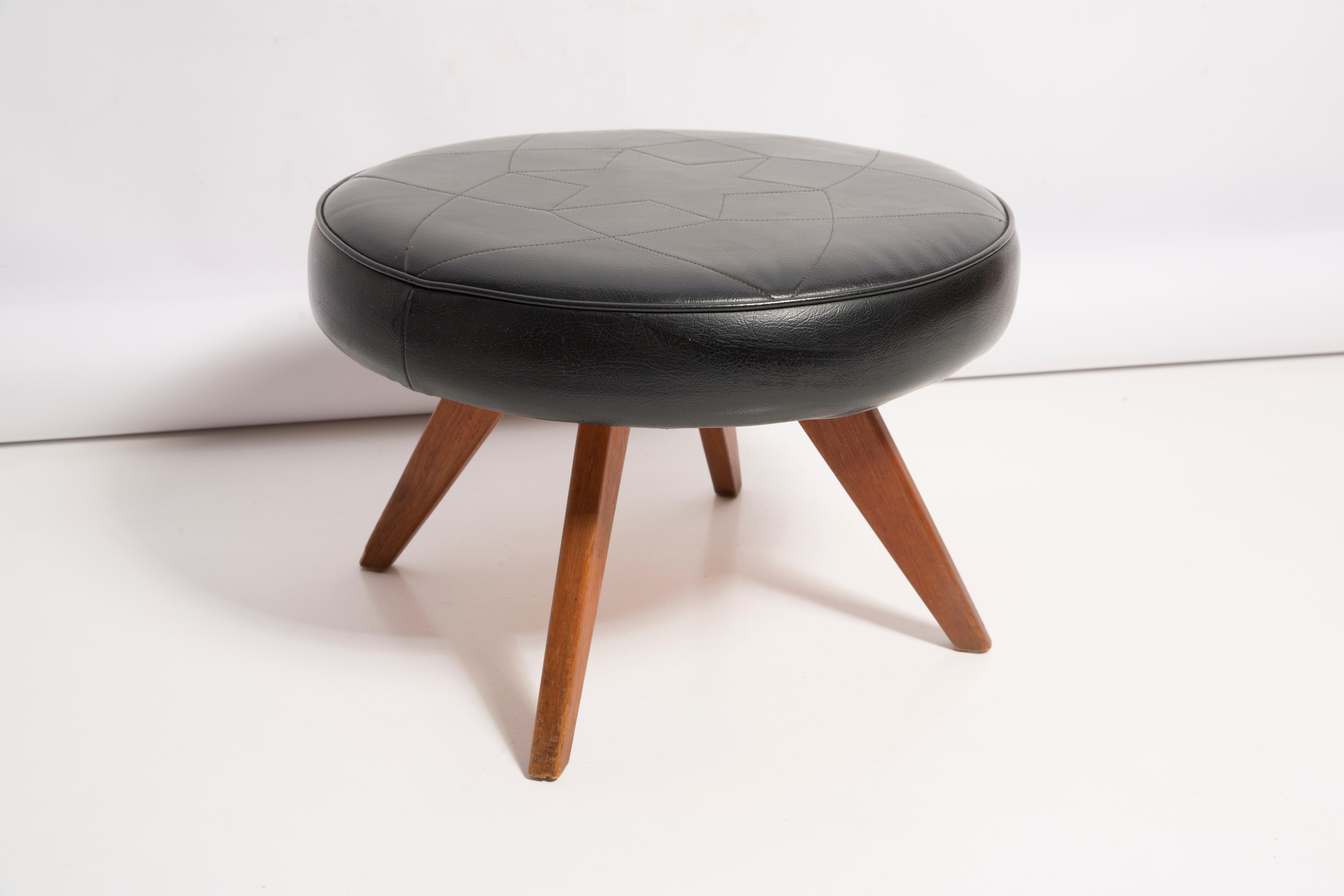 Stool from the turn of the 1960s. Beautiful black high quality faux leather. The stool consists of an upholstered part, a seat and wooden legs narrowing downwards, characteristic of the 1960s style. They are in good original vintage condition -