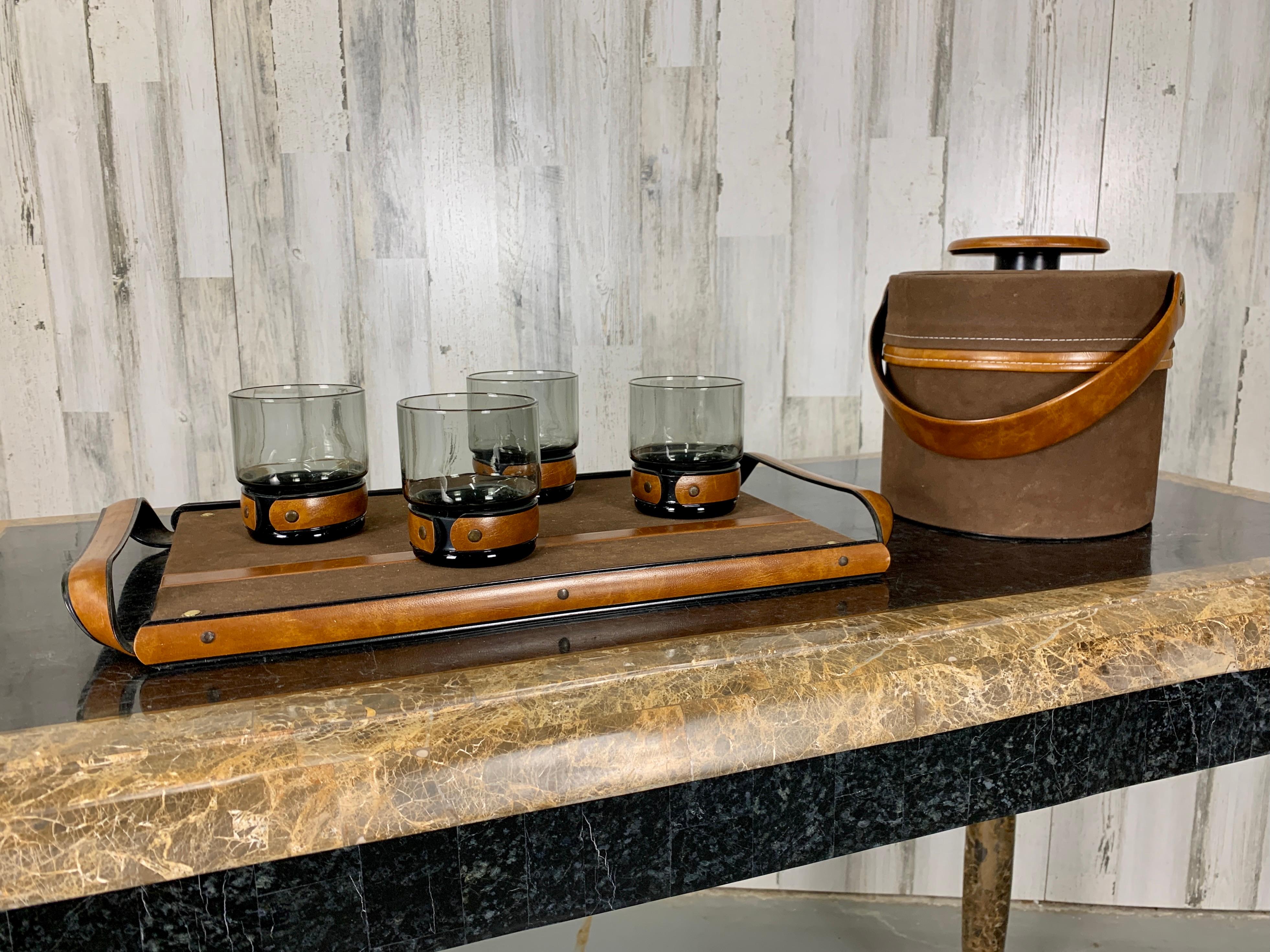 Four smoked glasses with faux leather banding with ice bucket and serving tray. Manufactured by Coordinated Barware

Tray: 19 1/4 W x 10 7/8 D x 1 5/8 H
Glasses: 3 1/4 Diam x 3 5/8 H
Ice Bucket: 8 7/8 D x 8 5/8 W x 8 1/4 H.