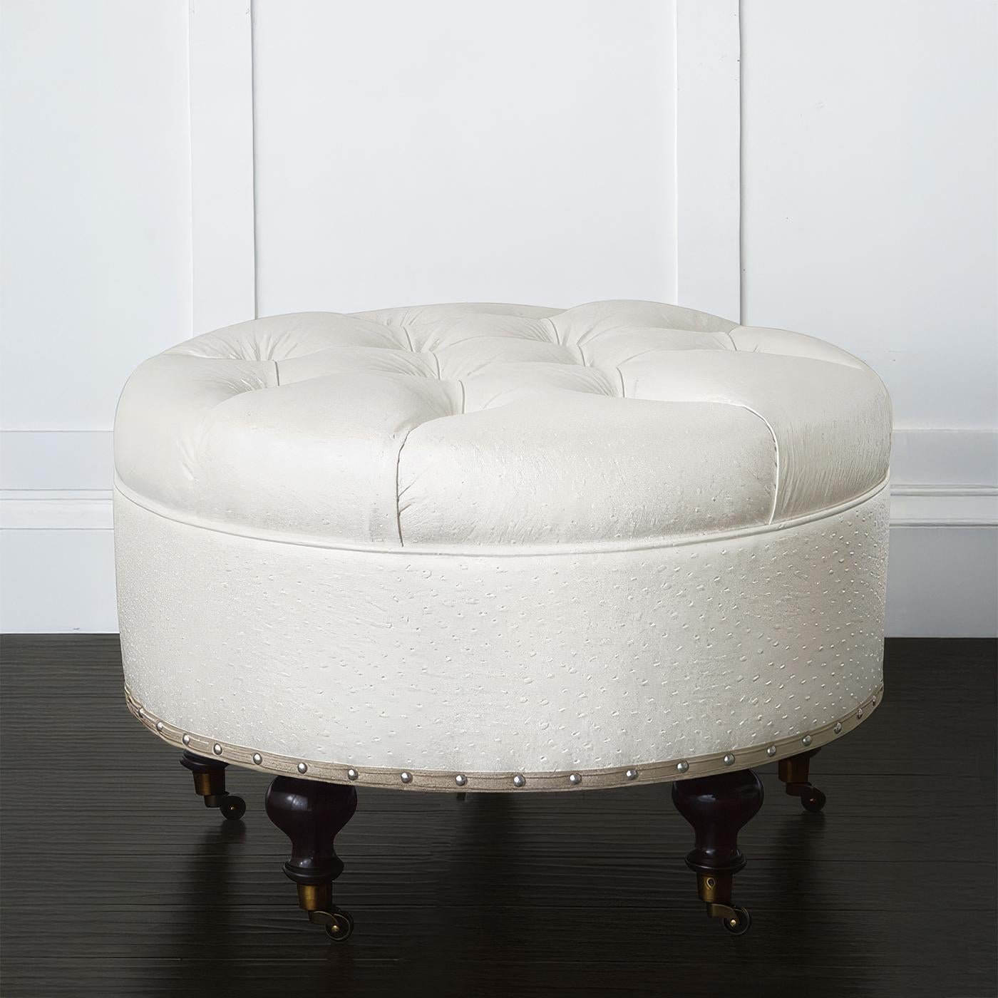 Realizzato negli Stati Uniti, questo pouf è caratterizzato da una profonda imbottitura a bottoni e da un rivestimento in finta pelle di struzzo color avorio metallizzato. Le piccole rifiniture auto-avvolgenti e le teste dei chiodi in nichel