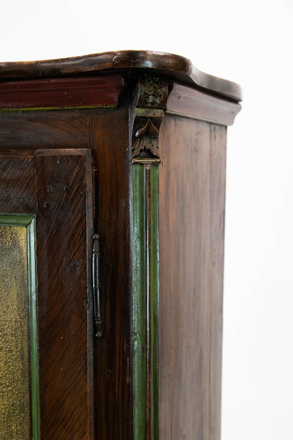 The door of this bonnetiere has fluted chamfered corners and is faux painted with herringbone banding. The shelves are fixed.