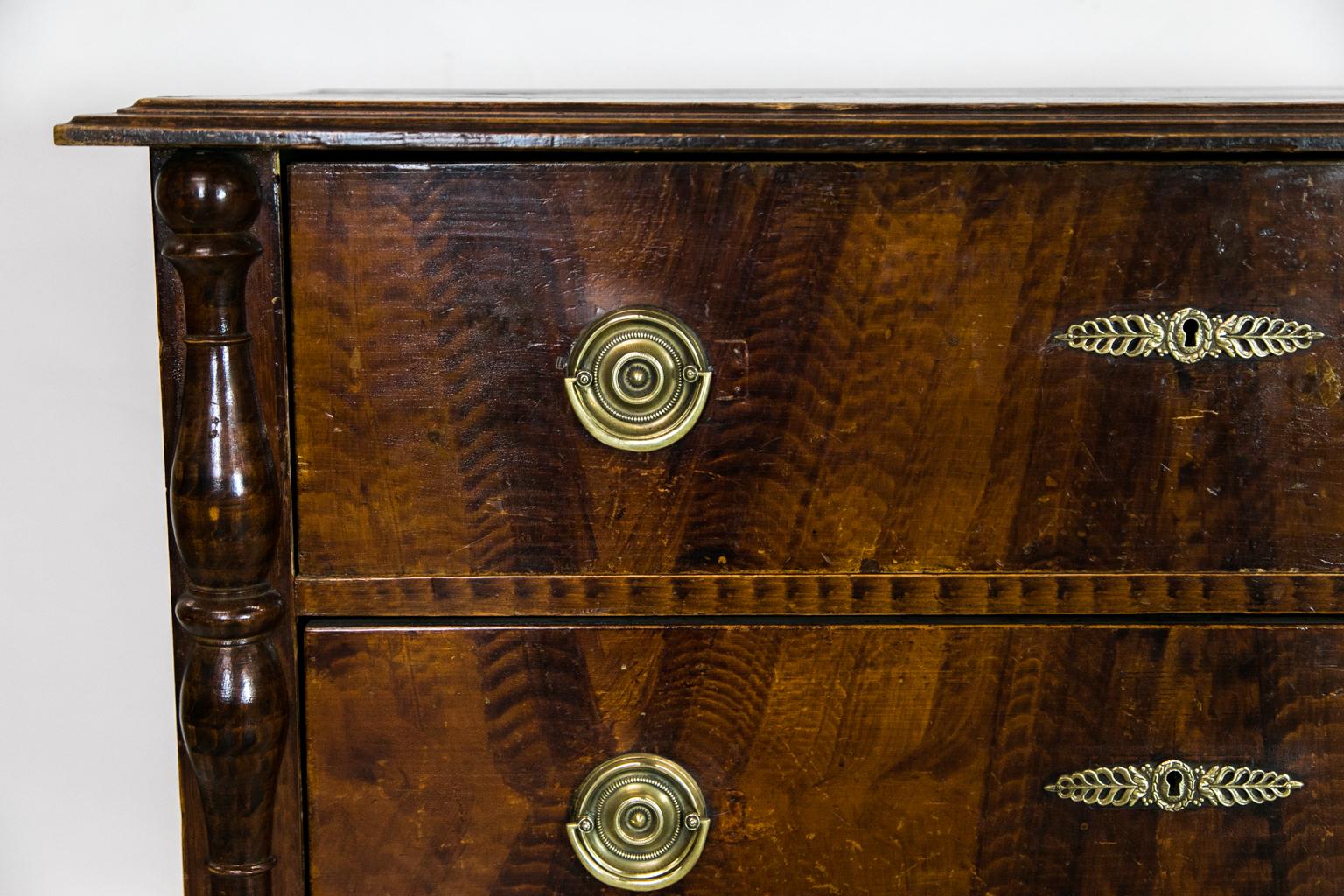 This faux painted commode/chest has faux grain throughout. The top has a deep molded edge. The stiles have applied split turnings and terminate in bun feet. The hardware is later.
