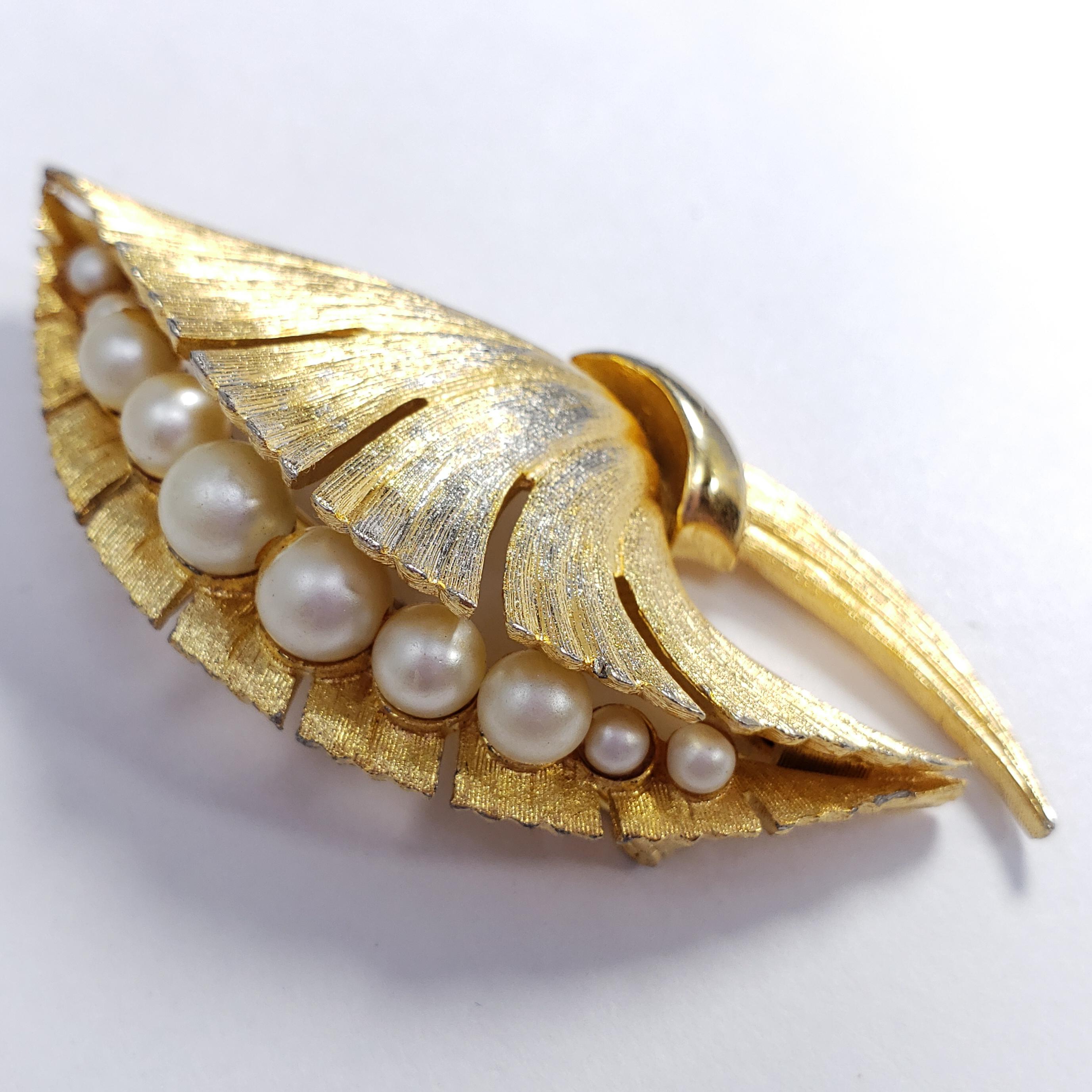 A vintage brooch by designer Sovereign. Features a line of faux pearls in a gold-plated bouquet-like motif. A classy accessory!

Some wear of gold plating is visible.
