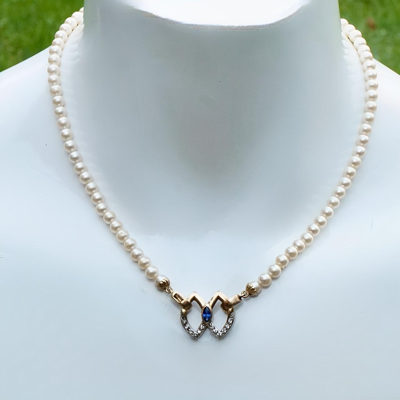 Ivory faux pearl necklace, featuring a lovely silver pendant with a gold wash. It has a blue glass centre stone, and is set with rhinestones on one side. The necklace closes with a clasp to the left. Measuring length 42.5 cm / 16.7 inches and the