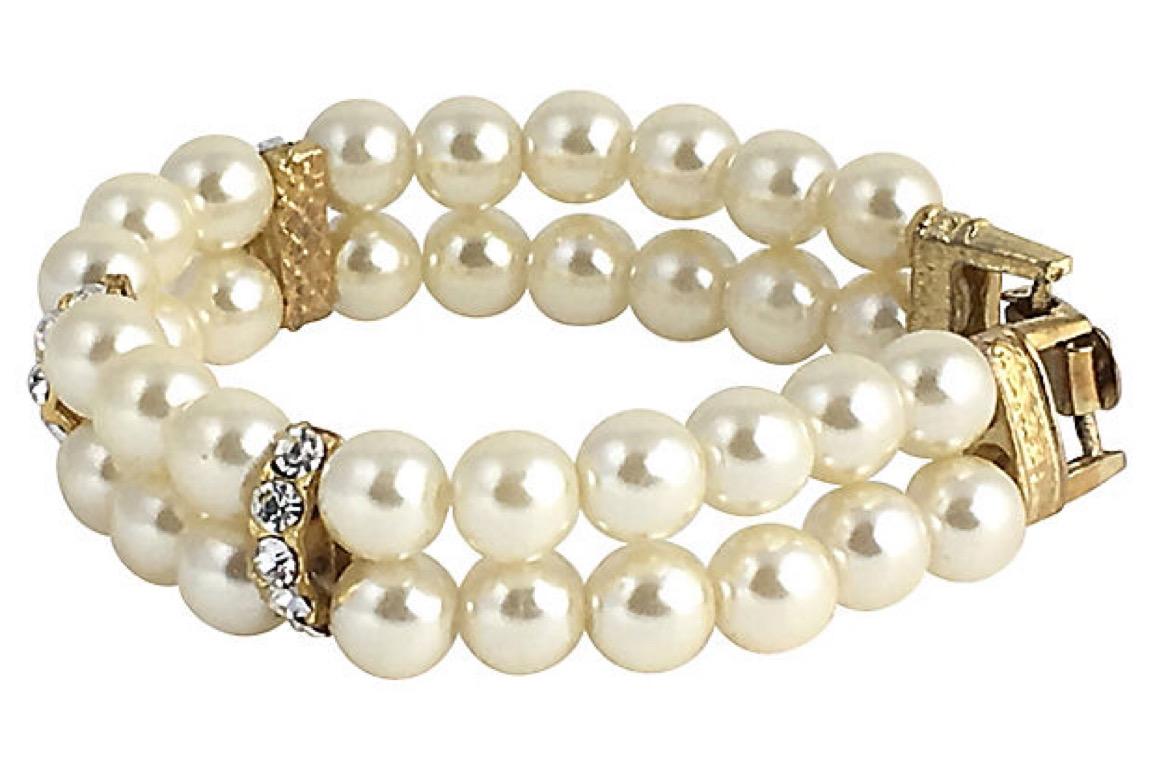 Double-strand faux-pearl bracelet interspersed with three spacer bars set with five rhinestones each. The goldtone metal is etched with a textured finish. Age wear, tarnish on clasp.