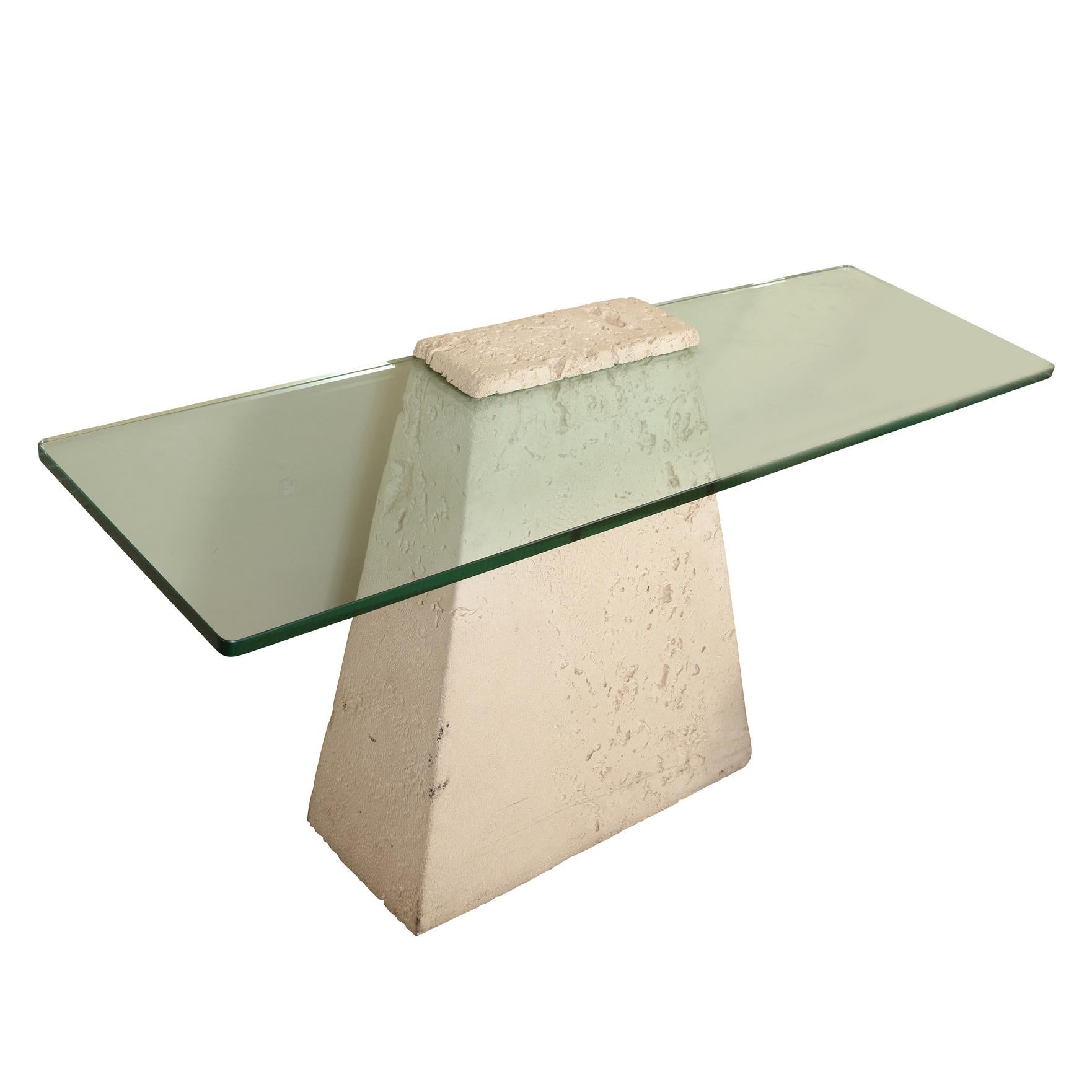A contemporary style console table with an angular faux stone base and a glass top.