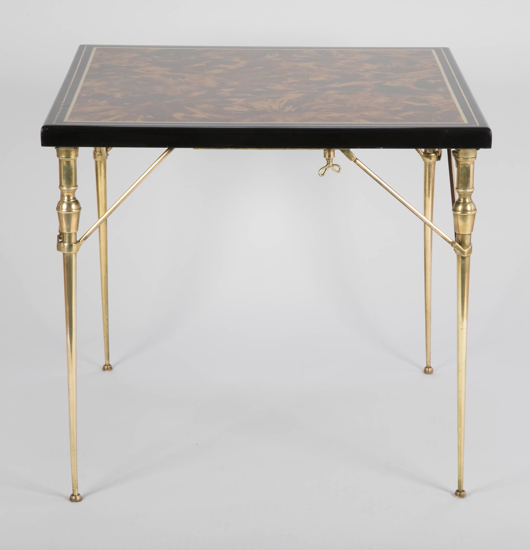 A stunning and possibly unique folding card or bridge table with a solid top of faux tortoise shell framed in black lacquer with a gilt edging. The bronze folding legs are beautifully crafted with and unusual turn-key locking mechanism. Clearly, a
