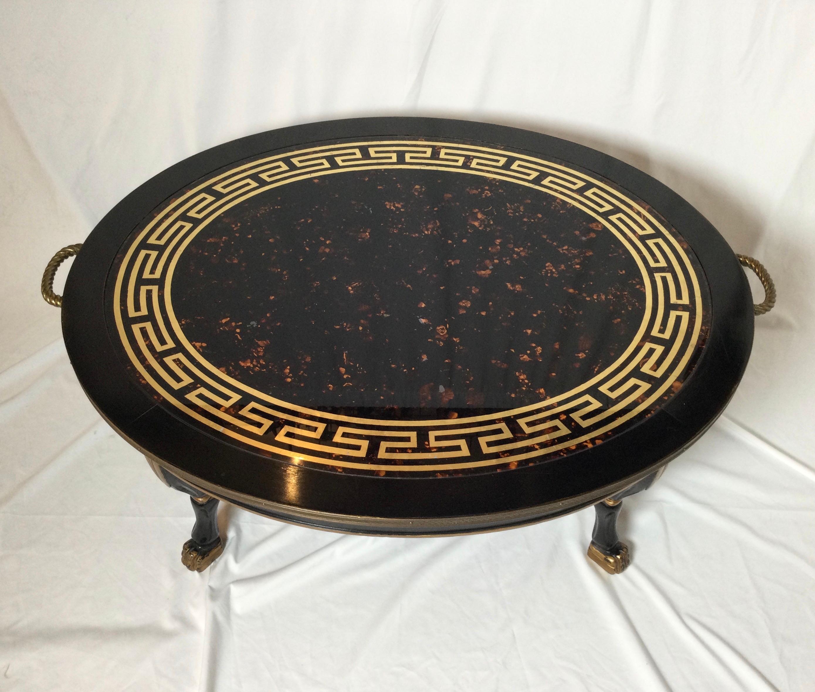 A faux tortoiseshell topped oval cocktail table with ebonized base. The top with gilt Greek key decoration with attached brass gallery edge and four gilt and ebonized legs with paw feet.