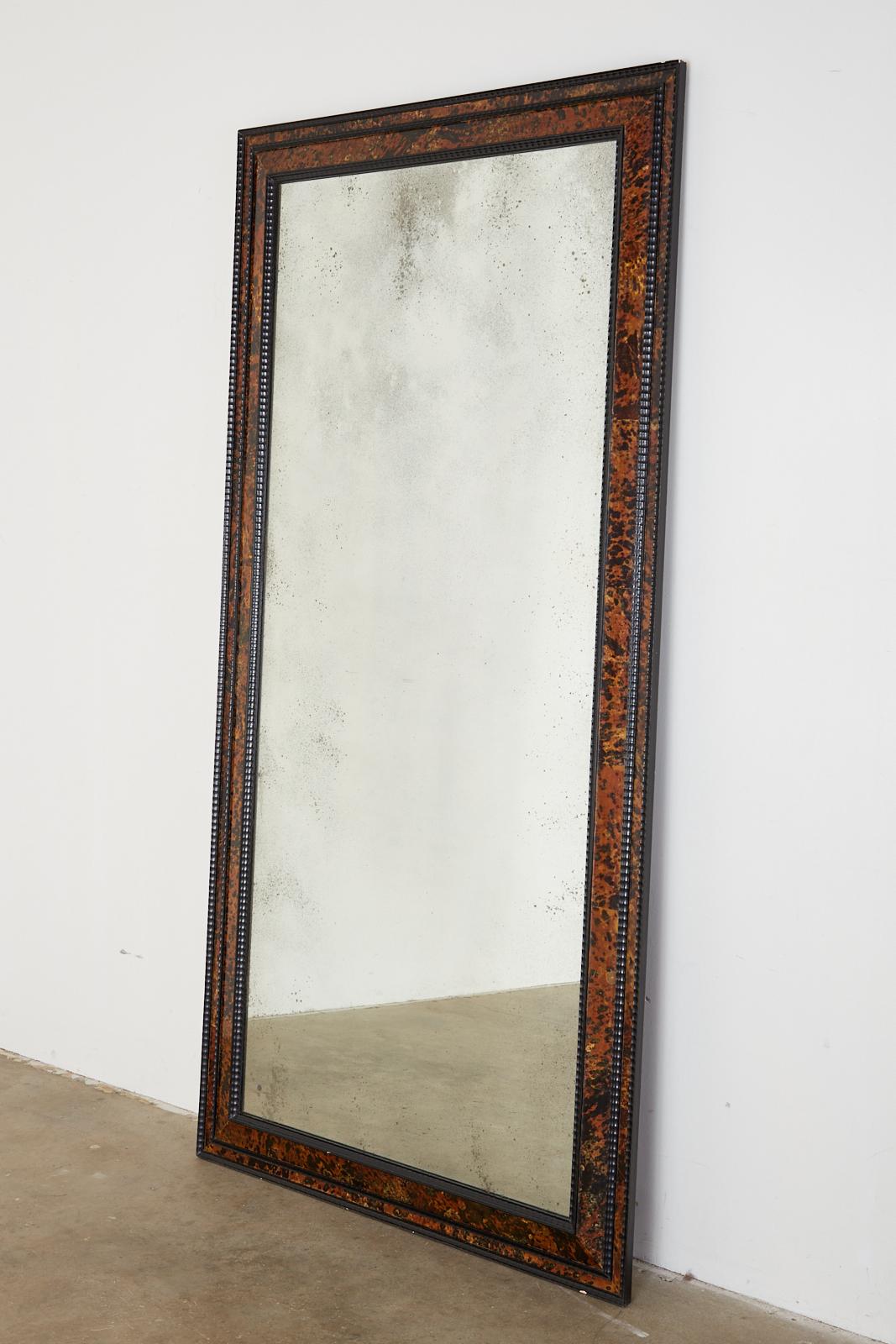 Fantastic faux tortoiseshell veneered floor mirror made in the Flemish or Dutch Baroque style. Features an exotic ebonized wood ripple frame with an inner and outer border that creates a dramatic look. The glass has an aged appearance of antique