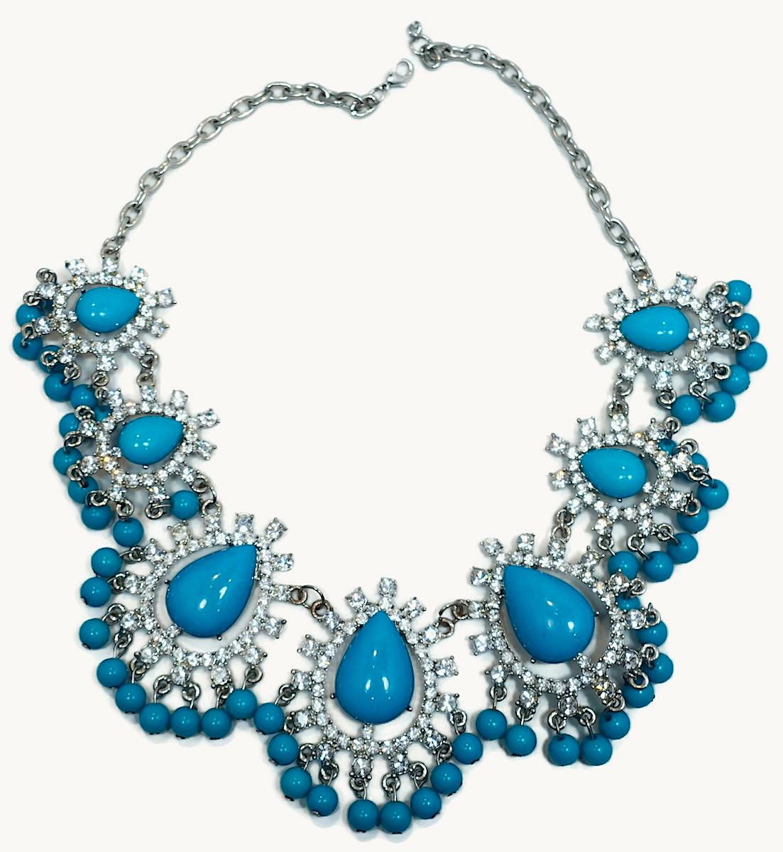 This stunning bib necklace has graduated cabochon pear-shaped faux turquoise stones surrounded with crystals and faux turquoise beads drops. It has a spring clasp connected to a silver tone chain.  The necklace measures 19” long with the front drop