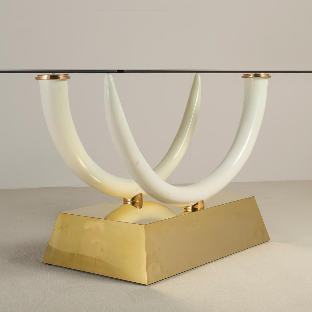 An unusual console table with faux tusks facing opposite directions and capped with brass to support a glass top (not included). The tusks are set on brass holders set upon a chunky polished brass base 1970s

Base measurements provided.