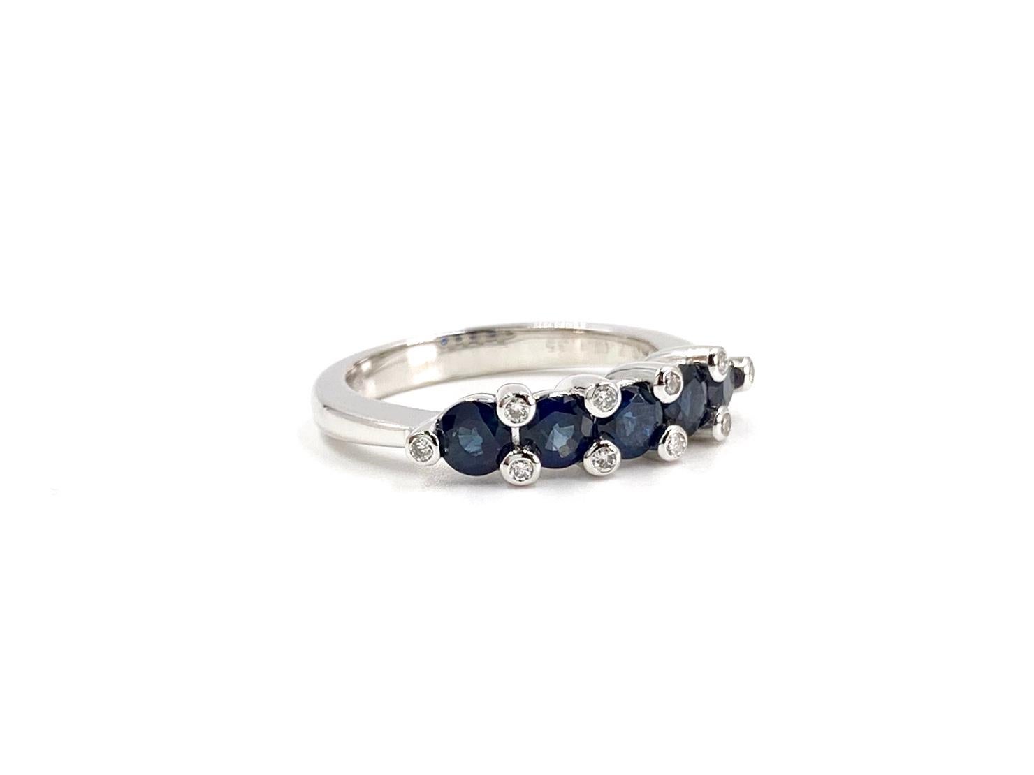 18 Karat white gold blue sapphire and diamond band ring by Favero. Five round deep blue sapphires have a total weight of 1.35 carats. Round diamonds are expertly bezel set within the prongs at .12 carats total weight. Width of face of band measures