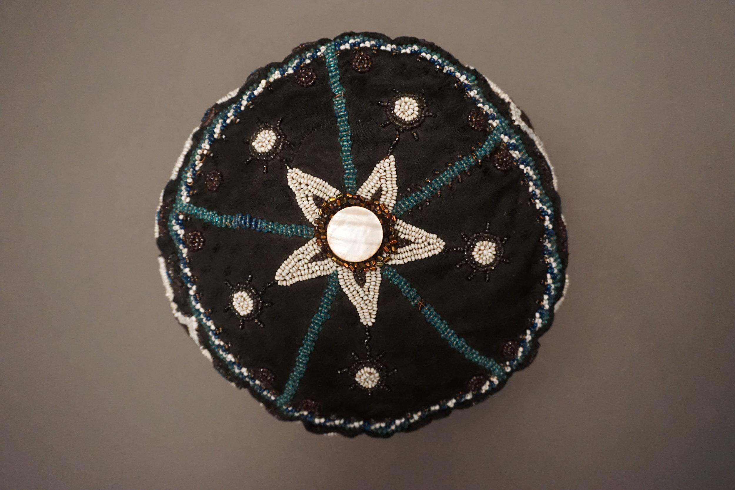 Region / Tribe: Kansas/ Nebraska border/ Otoe-Missouria
circa 1891-1895
Material: Various cloths, glass beads, cotton thread, shell disk
Dimension: Diameter 10 inches, height 2 3/4 inches 
Condition: Overall excellent. Minor bead loss along