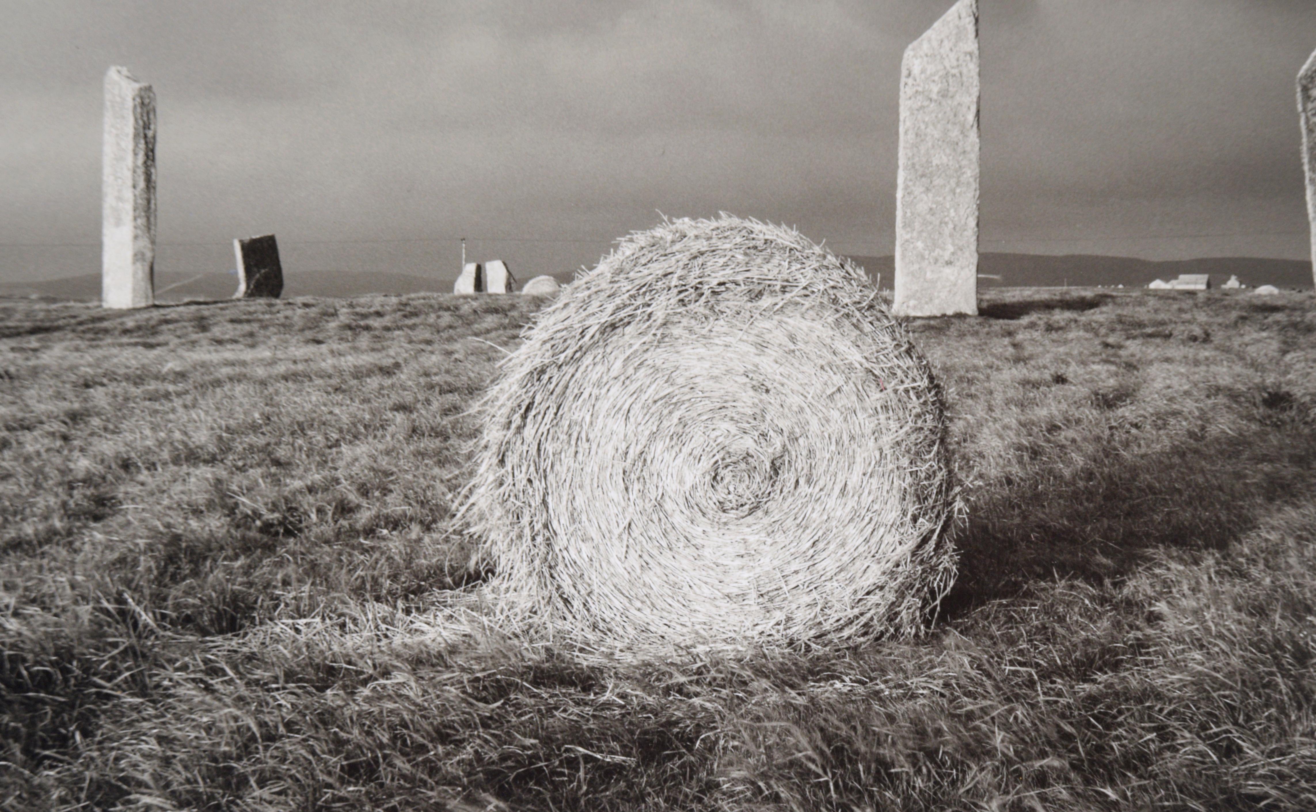 Splendida fotografia in bianco e nero di Fay Godwin (Regno Unito, 1931-2005). Questa fotografia è stata scattata alle Stones of Stennes nelle Orcadi, in Scozia, nel 1985. Un rotolo di fieno è il fulcro dell'opera, con le pietre sullo sfondo e un
