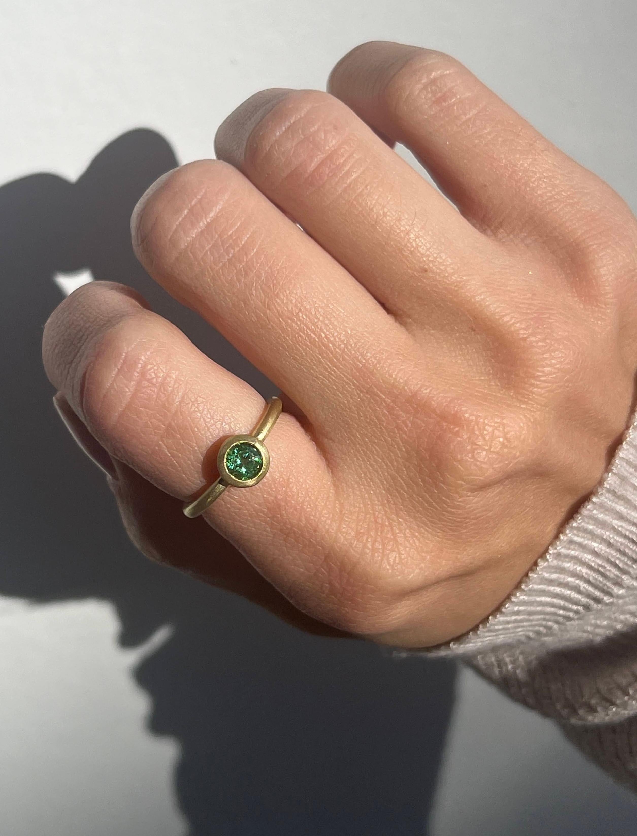 L'anello con castone rotondo con tormalina verde in oro 18 carati di Faye Kim, dal colore verde bluastro trasparente e brillante, è splendidamente incastonato e rifinito in modo opaco. L'anello può essere indossato da solo o impilato con altri