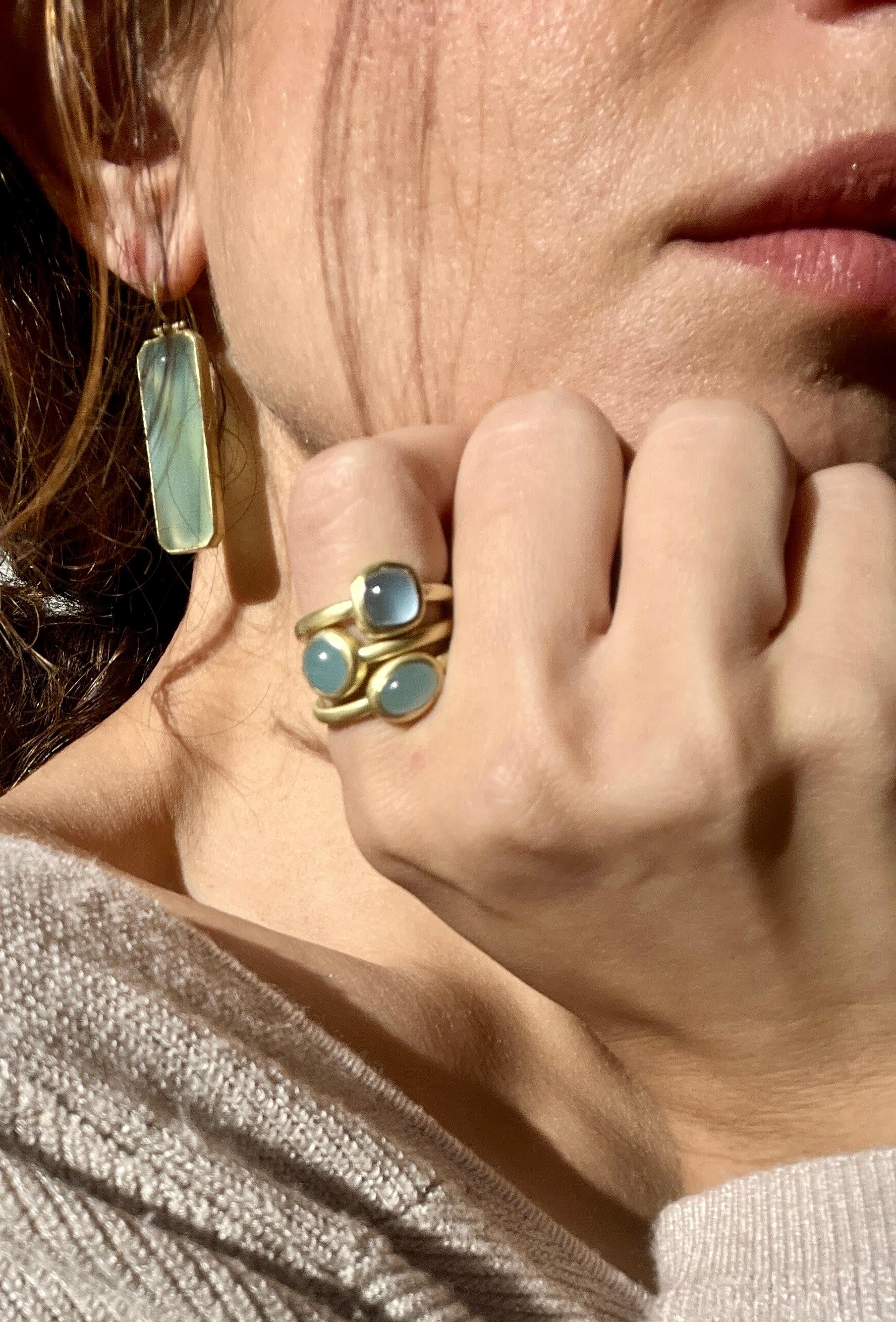 Faye Kim's beautiful Milky Aqua Bezel Ring is handcrafted in 18 karat gold. The clean bezel setting, cushion-cut shape, and matte gold finish enhance the stone's natural blue-gray color. Wear alone or stacked with other rings for a stylish, modern