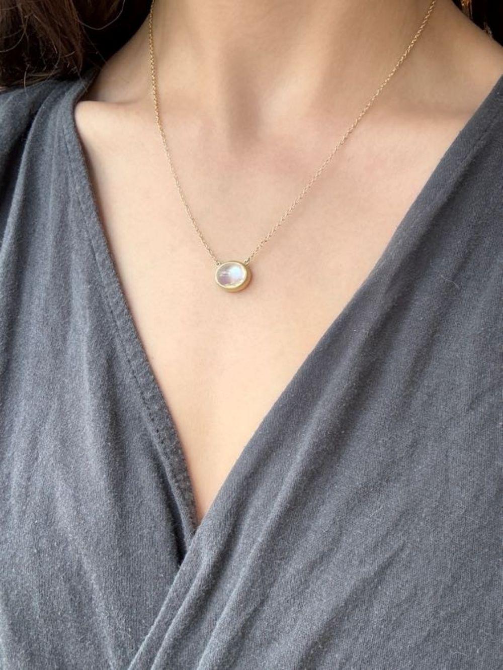Faye Kim's 18 Karat Gold Oval Moonstone Pendant Necklace, attached to a 1.5mm cable link chain, is full of light and reflects beautiful translucent hues. The shape, polish, and matte gold finish enhance the moonstone's striking rainbow effect while