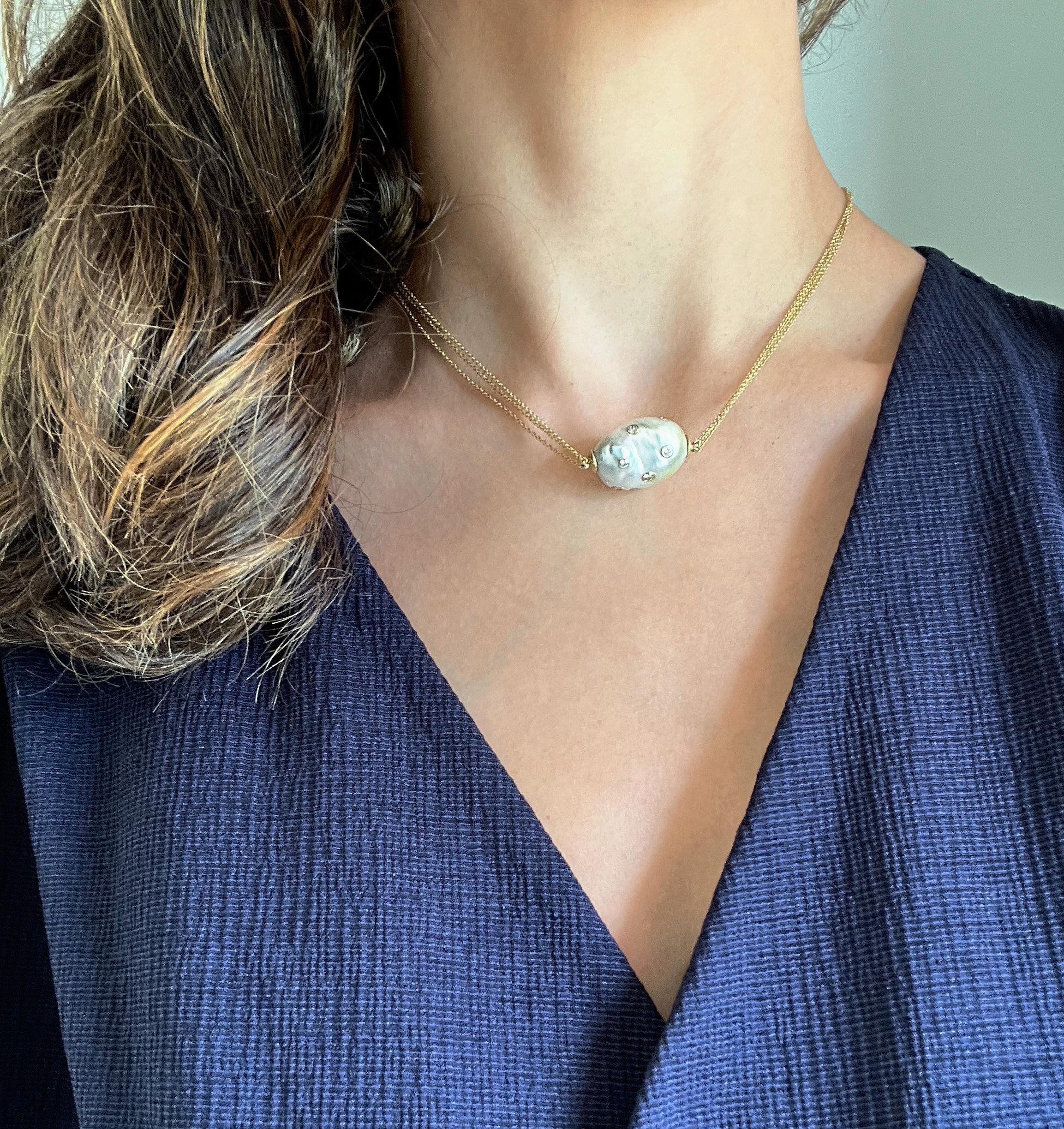 Unique and hard to find, an oversized, baroque white south sea pearl is studded with round brilliant cut diamonds.  Each diamond is bezel set and hangs on a triple strand cable chain necklace, all in 18k gold. The pearl has a silver overtone with a