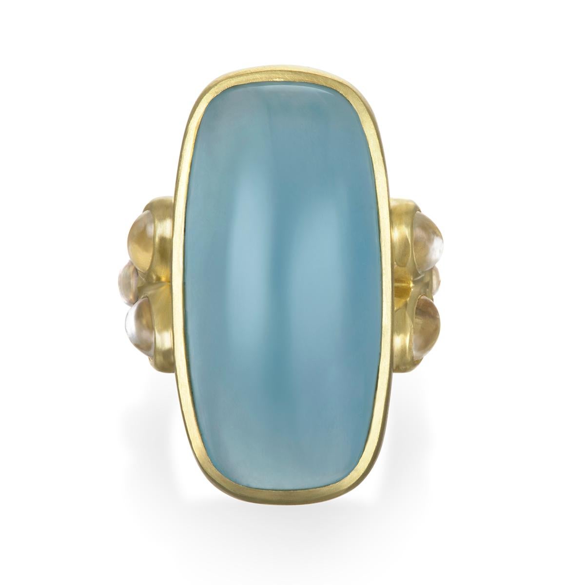 Faye Kim's signature 18k gold setting is perfect for this oversized milky Aquamarine cabochon coming in at over 32 carats.  Flanked with triple oval moonstones give it a breath of lightness and iridescence.  A beautiful and modern look that is great