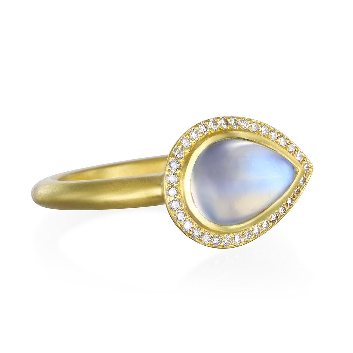 This beautiful Moonstone Bezel Ring is full of light and reflects beautiful translucent blue hues. The shape, polish, and matte gold enhances the moonstones striking rainbow effect. Complete with a Diamond halo for extra sparkle.

Handcrafted in 18k