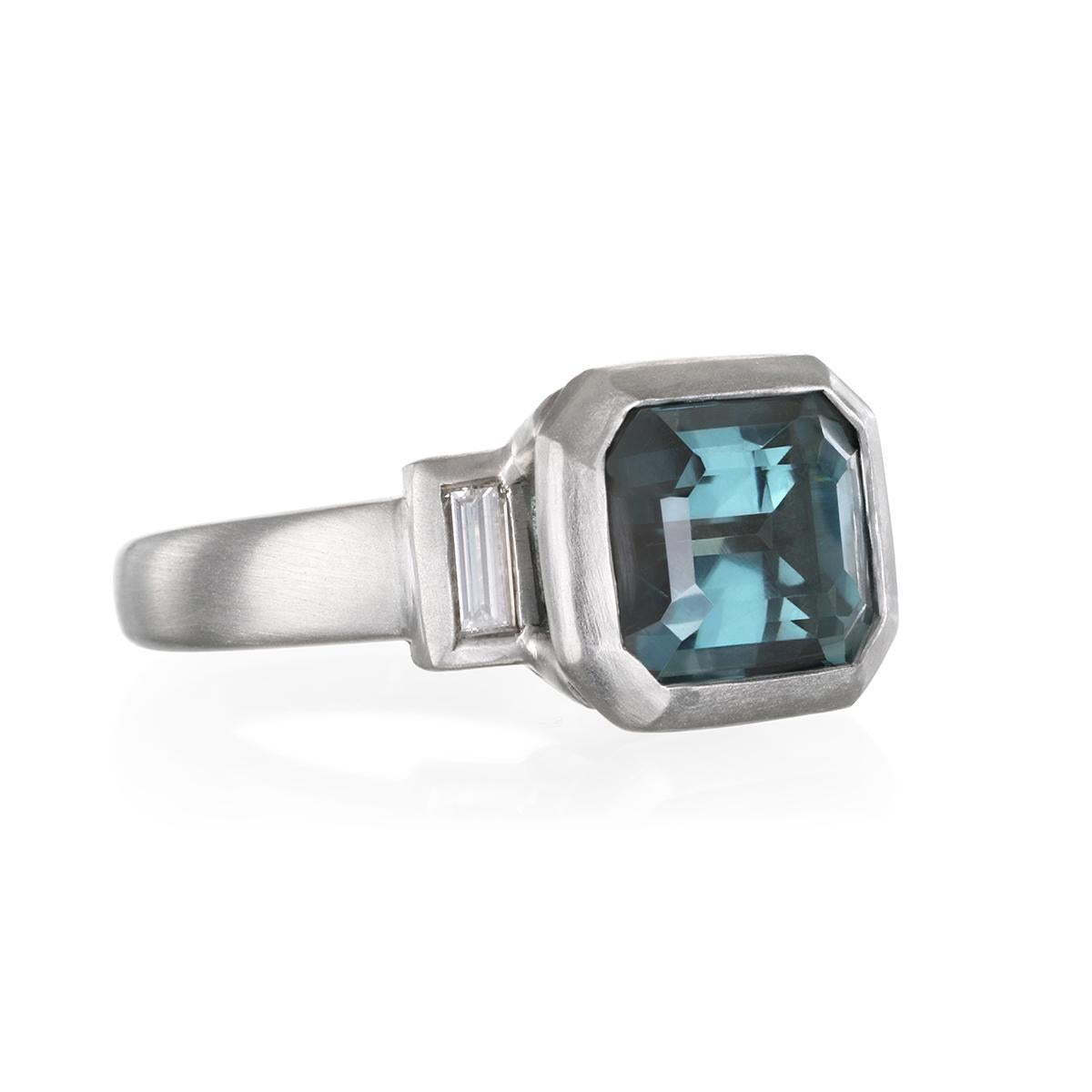 A rich shade of blue-green, this emerald-cut Tourmaline is flanked by two diamond baguettes. Powerful, sleek in a robust matte-finished platinum setting.  A stunning, one-of-a-kind statement piece.

Blue Green Tourmaline: 6.20 Carats
Diamonds: .37