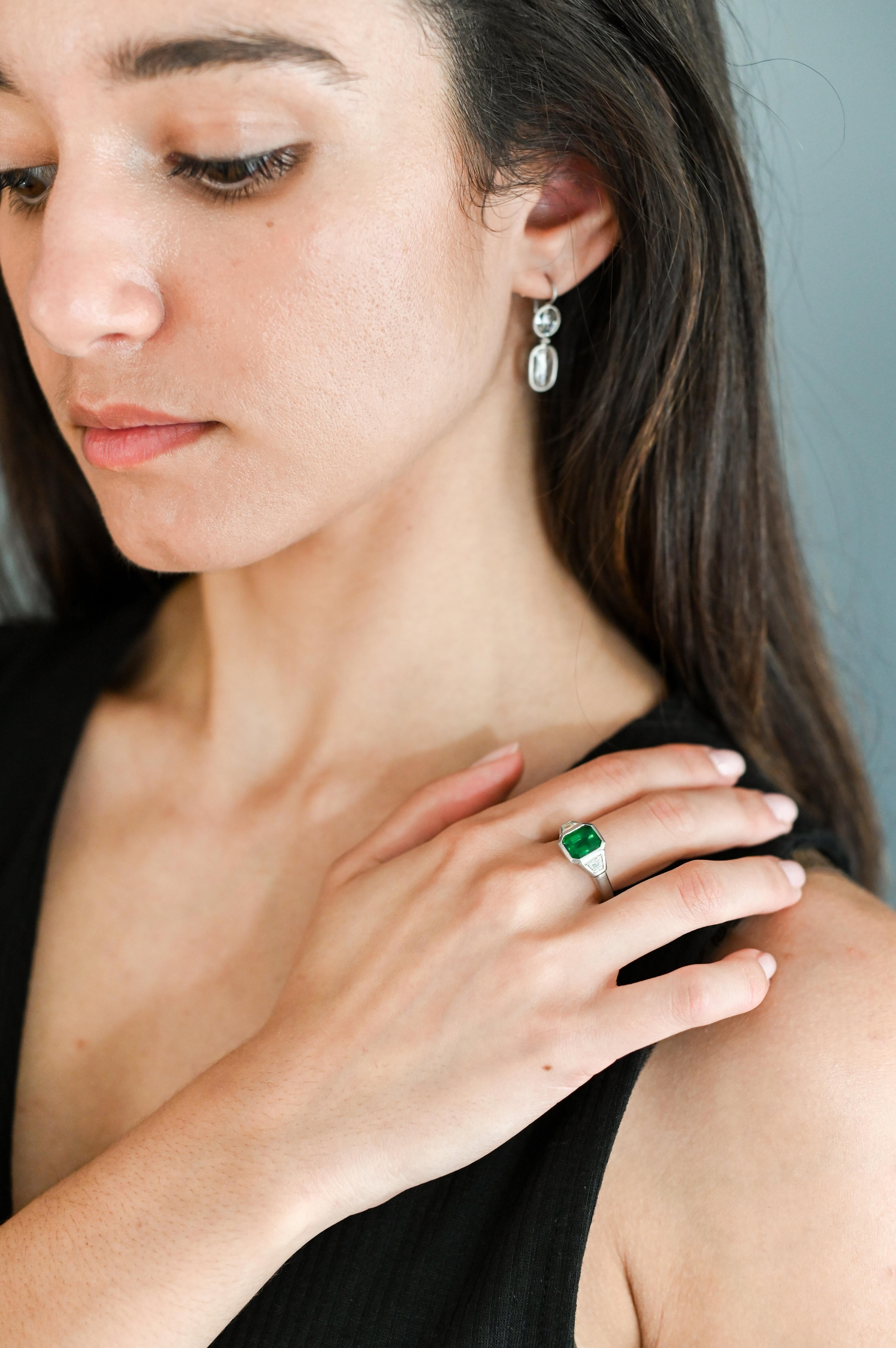 Timeless Three Stone Emerald and Diamond Bezel.  Set in Platinum and beautifully crafted, the Brazilian Emerald is flanked by diamond trapezoids, highlighting the deep, beautiful green hue.

Ring Size 7
LxW - 10.2 x 9.8MM
Brazilian Emerald - AGTA