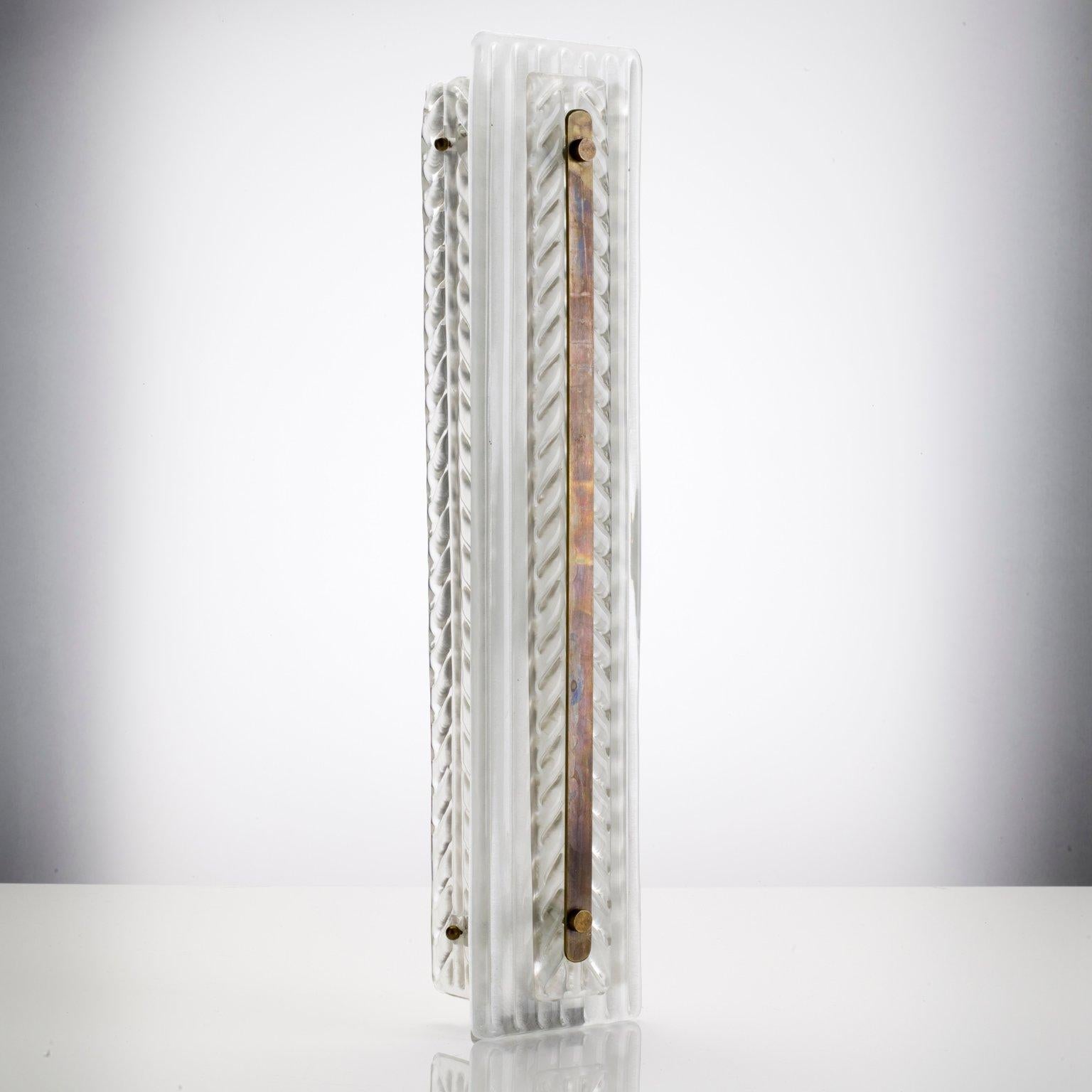 Produced from original Murano glass fixed to a white powder coated frame. The front glass is ribbed with an appliqué with feather style detailing. A brass strip runs the length of the front. Brass finger screws hold the glass to the frame behind.