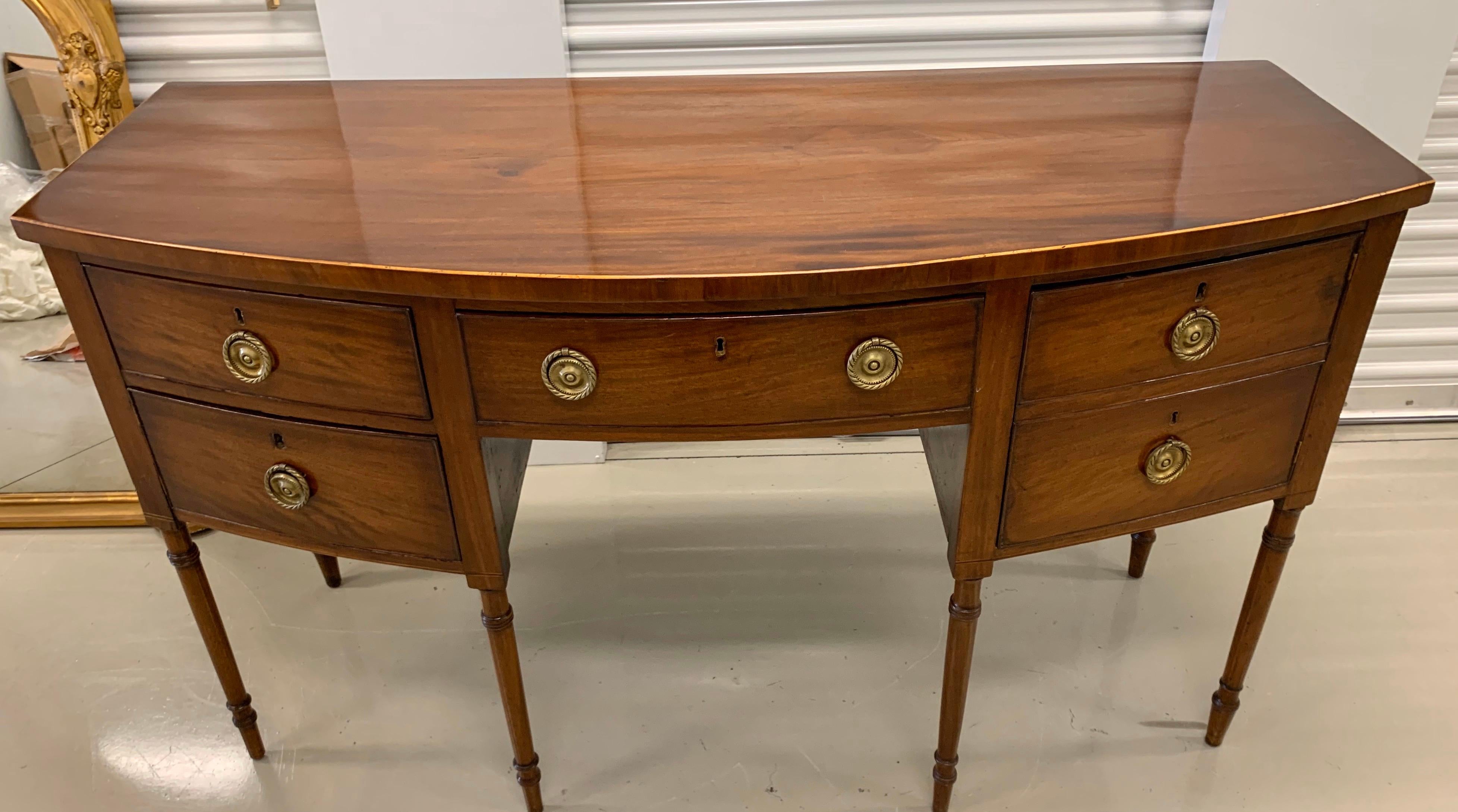 Elegant Federal antique mahogany bow front sideboard with multiple drawers. There are keys in the drawers, circa late 18th century with beautiful aged patina. Original hardware with lock and keys.
Left top drawer locking mechanism is stuck.