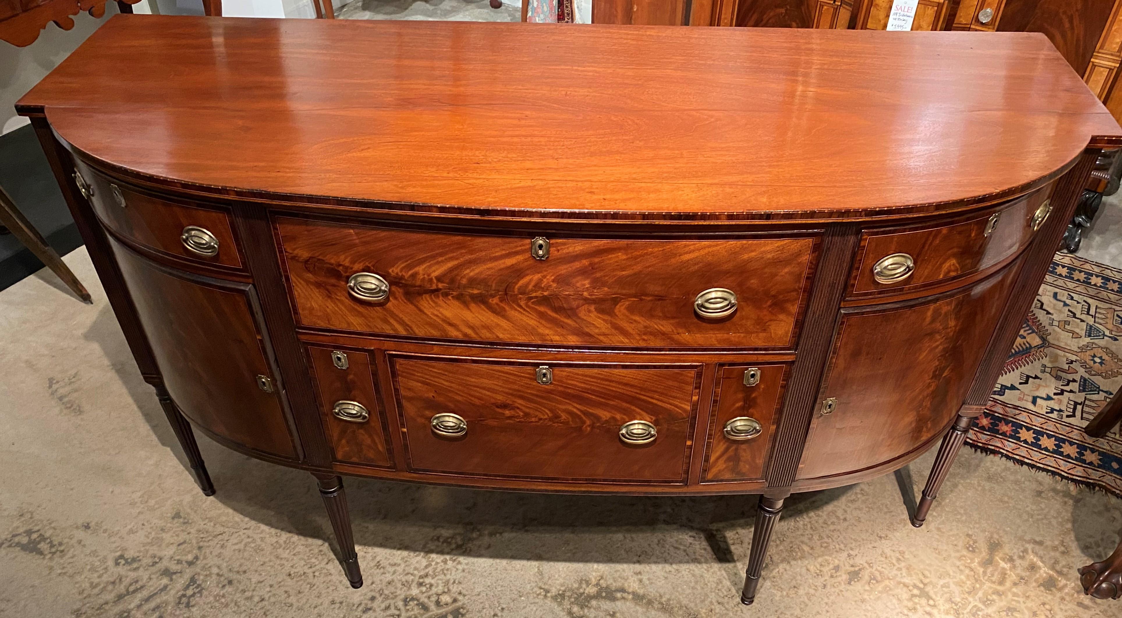An exceptional Federal Boston demilune Mahogany sideboard, with shaped top with delicate arrow inlay surmounting a conforming case with deep central frieze drawer flanked by smaller fitted felt lined flatware drawers, over a second deep center