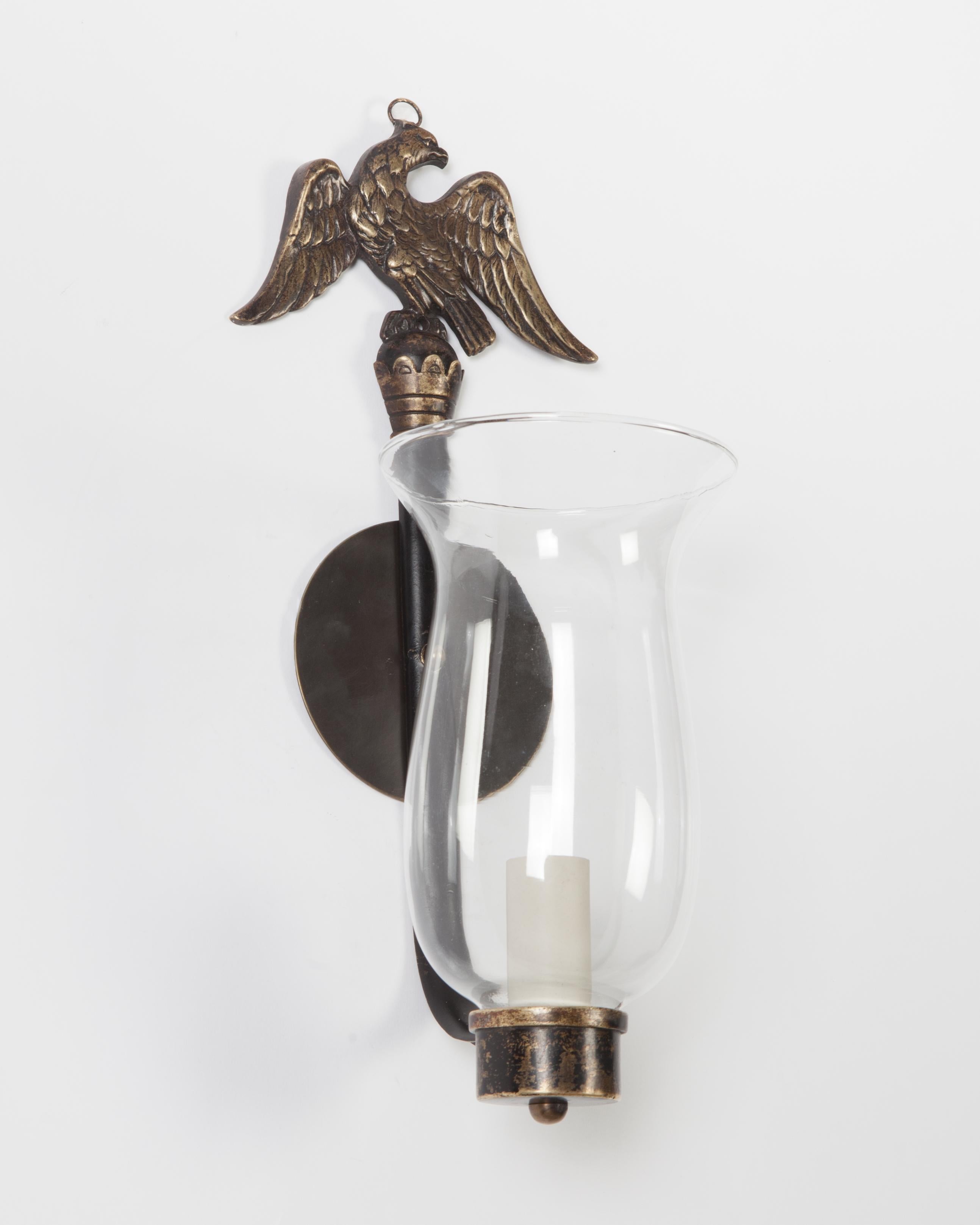 AIS2912
A pair of single light federal Revival period sconces with clear glass hurricane shades and slender backplates surmounted by eagles, circa 1920. Retaining their aged brass and worn black lacquer finish. There may be some nicks or