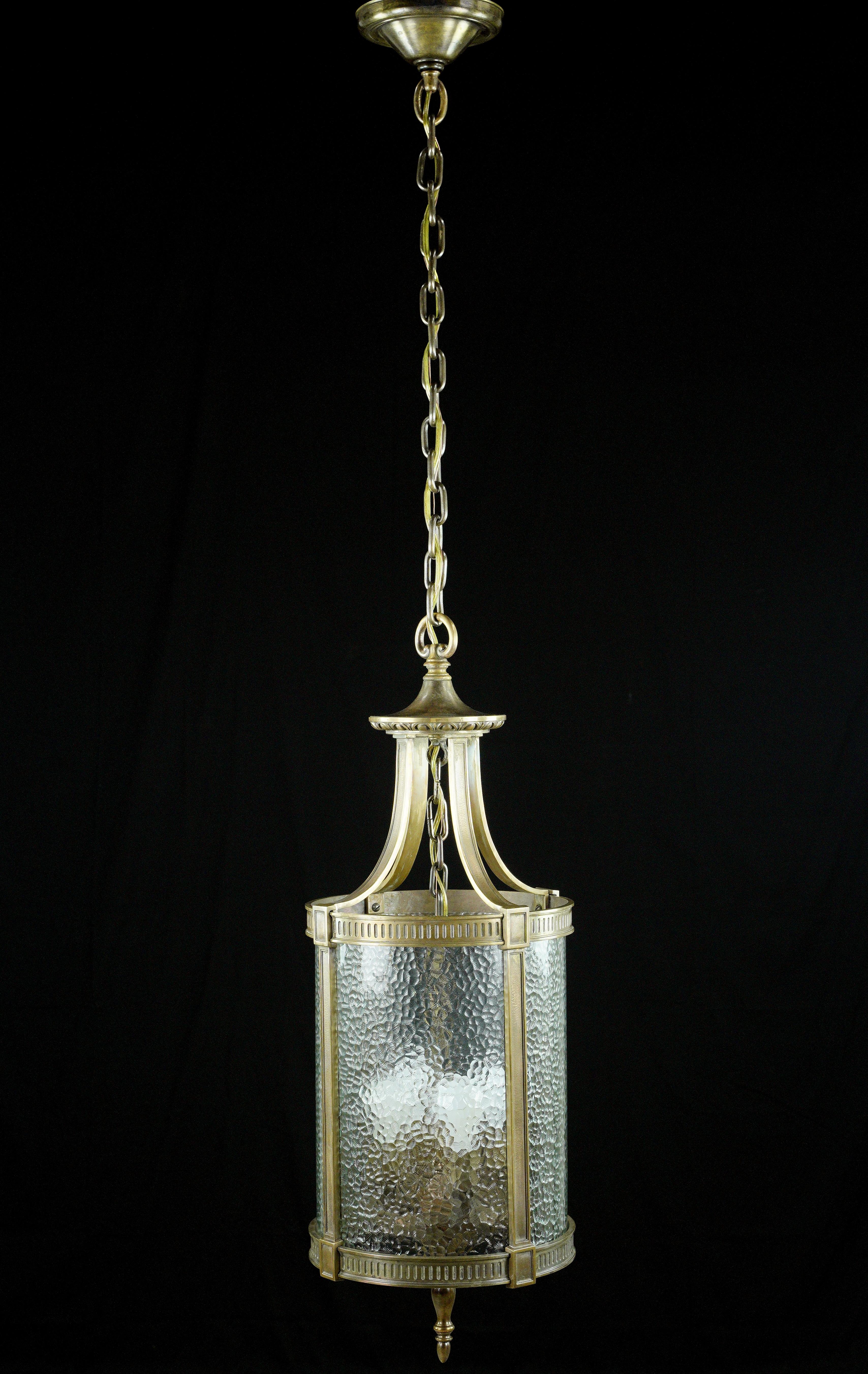This early 20th Century hanging lantern exudes timeless charm. Its bronze frame and clear pebbled glass showcase a classic design, capturing the essence of the Federal style, making it a captivating lighting fixture for any inspired interior. This